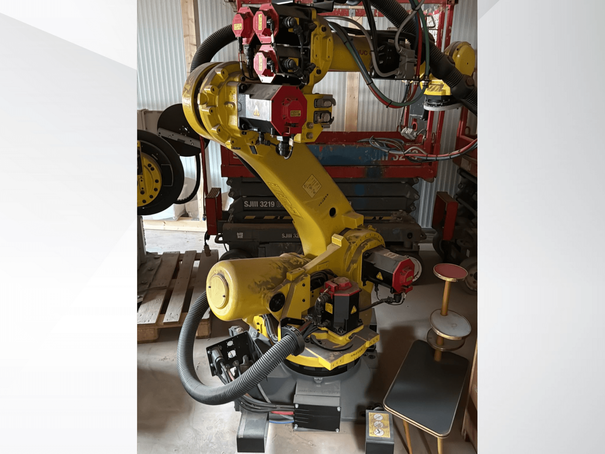 Bras robotique industriel jaune avec contrôleurs rouges, vue de face ; comporte de multiples articulations et tuyaux, placé sur un chantier.