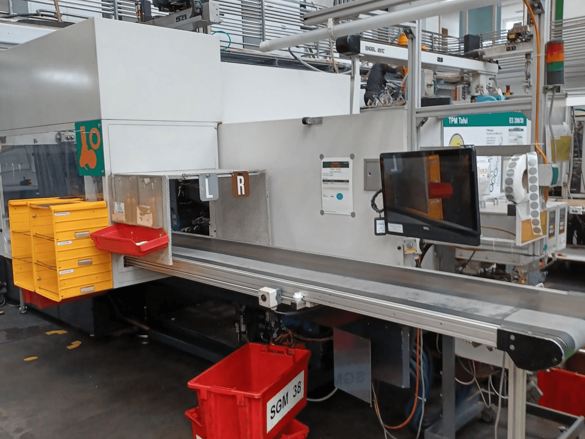 Machine de triage industrielle avec des bacs jaunes et rouges, vue de côté, comportant un écran de contrôle et des compartiments étiquetés pour le triage.