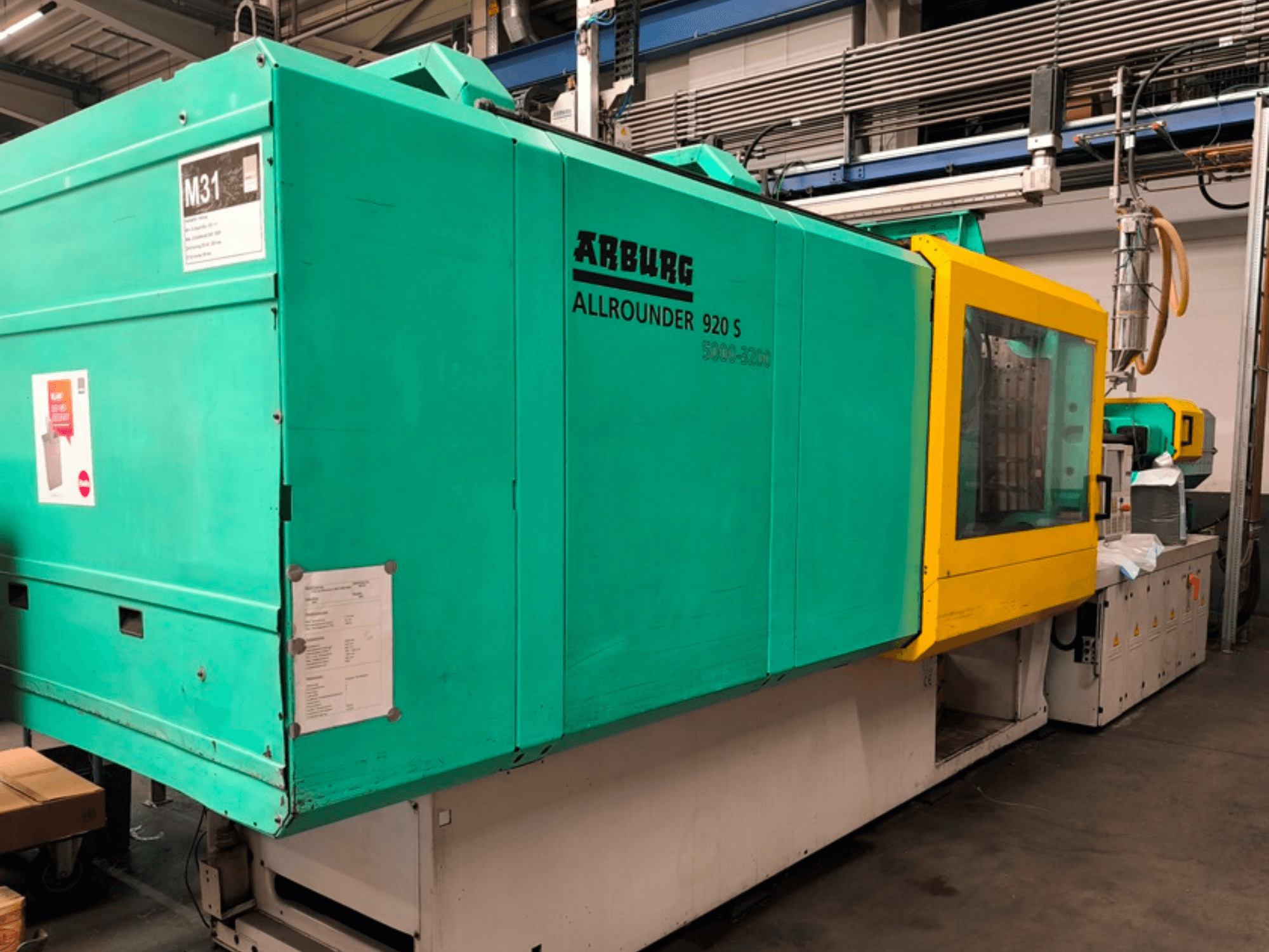 Machine de moulage par injection Arburg Allrounder 920 S en bleu aqua et jaune, vue latérale montrant le panneau de commande et les composants.