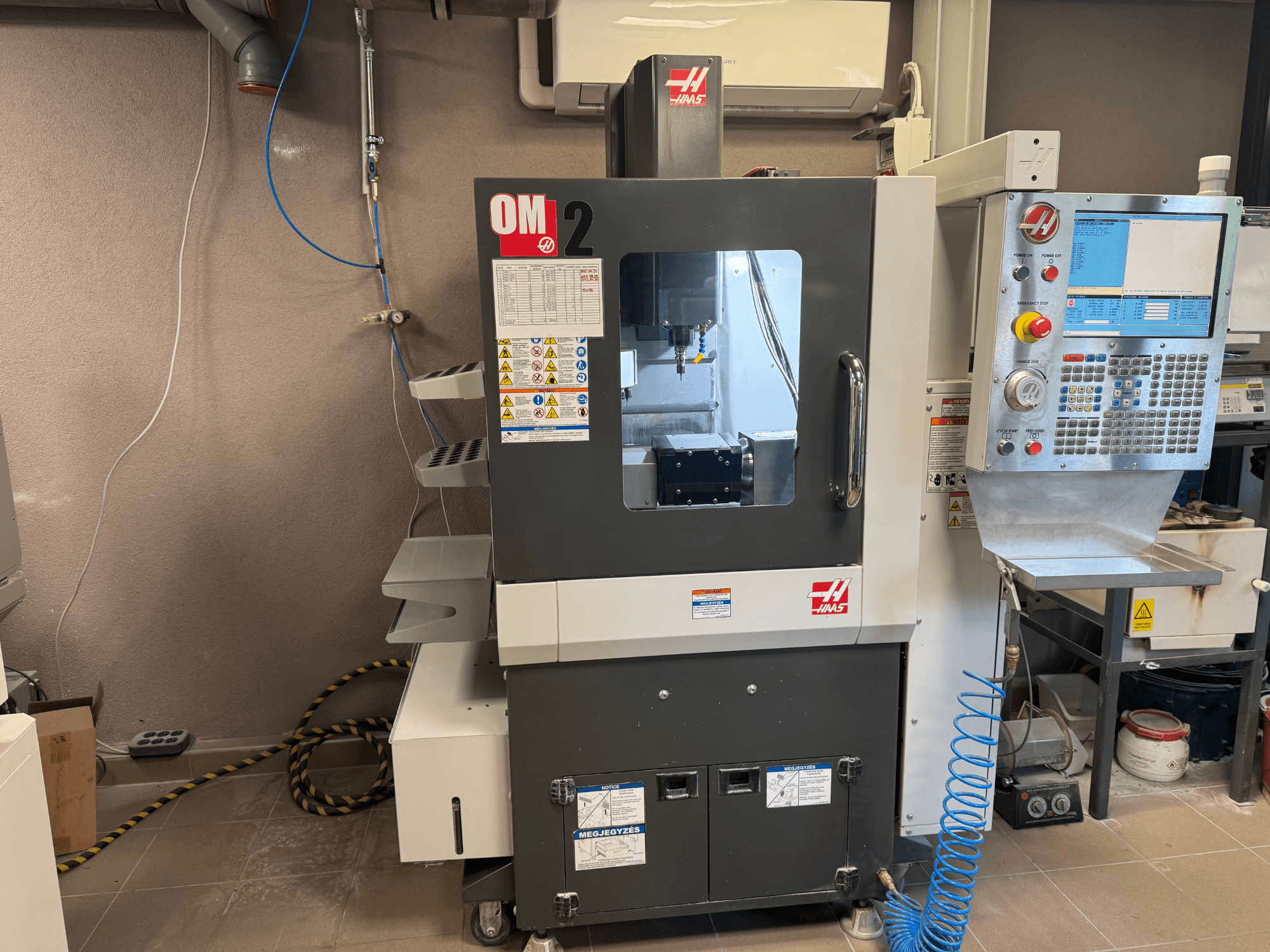 Machine CNC Haas OM-2, vue de face, avec panneau de commande, broche et étiquettes de sécurité, dans un environnement d'atelier.