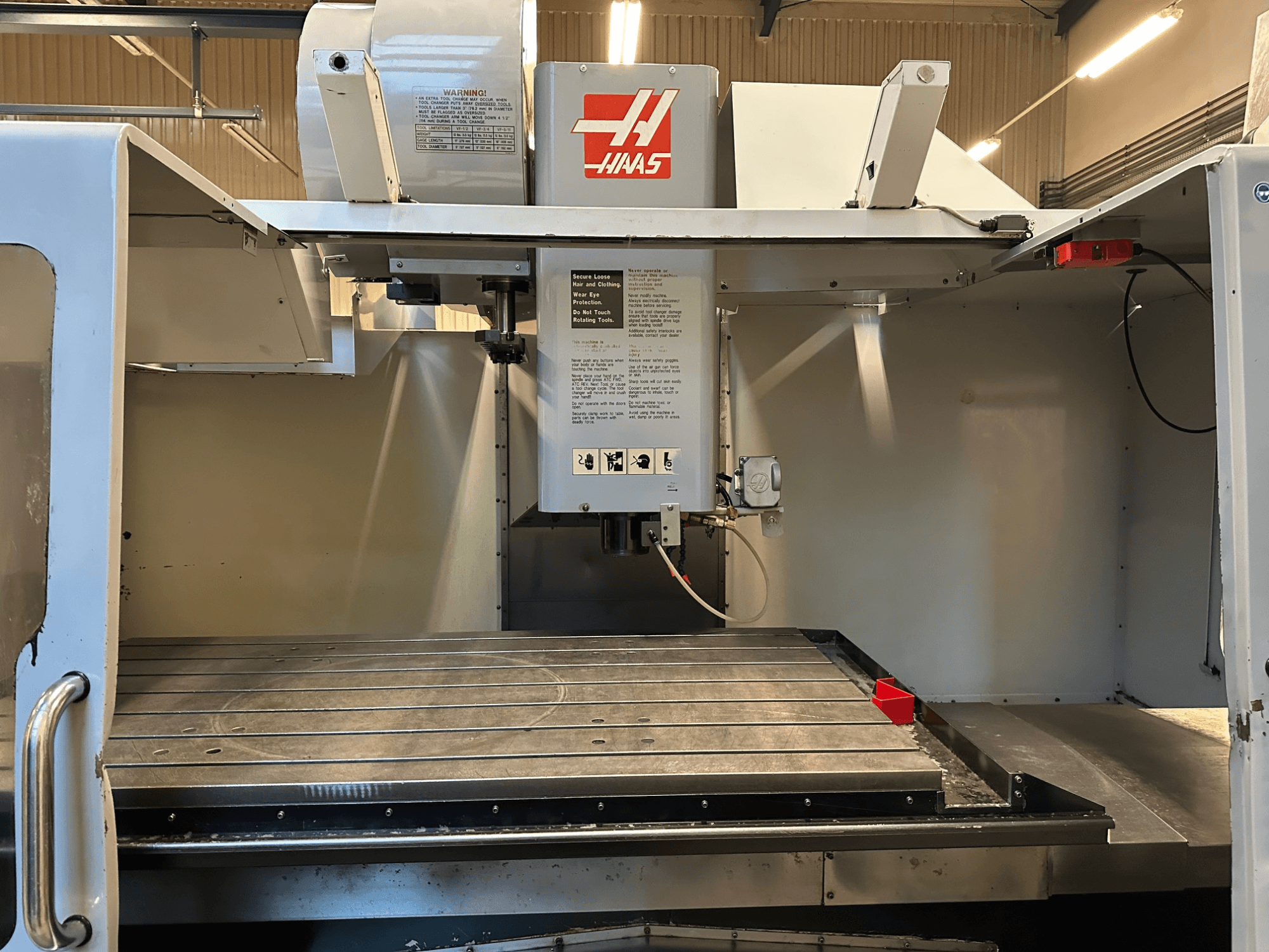 Fraiseuse CNC Haas, modèle VF-2, vue de face montrant les commandes, la table de travail en métal et l'étiquette de sécurité sur le panneau.