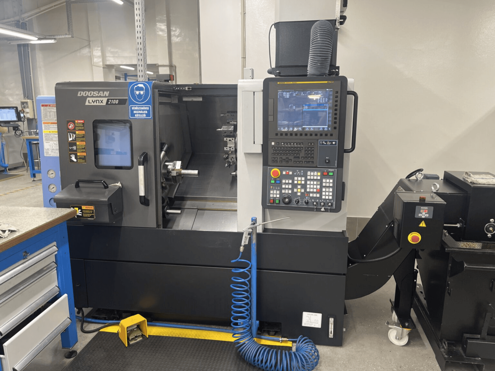 Vue avant d'un tour horizontal DOOSAN Lynx 2100A, montrant le panneau de commande et la zone de la broche avec des caractéristiques de sécurité notables.