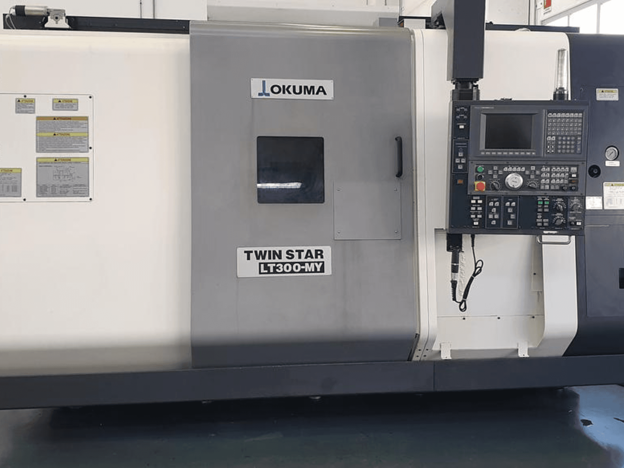 Tour CNC Okuma Twin Star LT300-MY en vue latérale, avec panneau de commande, boutons opérationnels et étiquettes de sécurité.