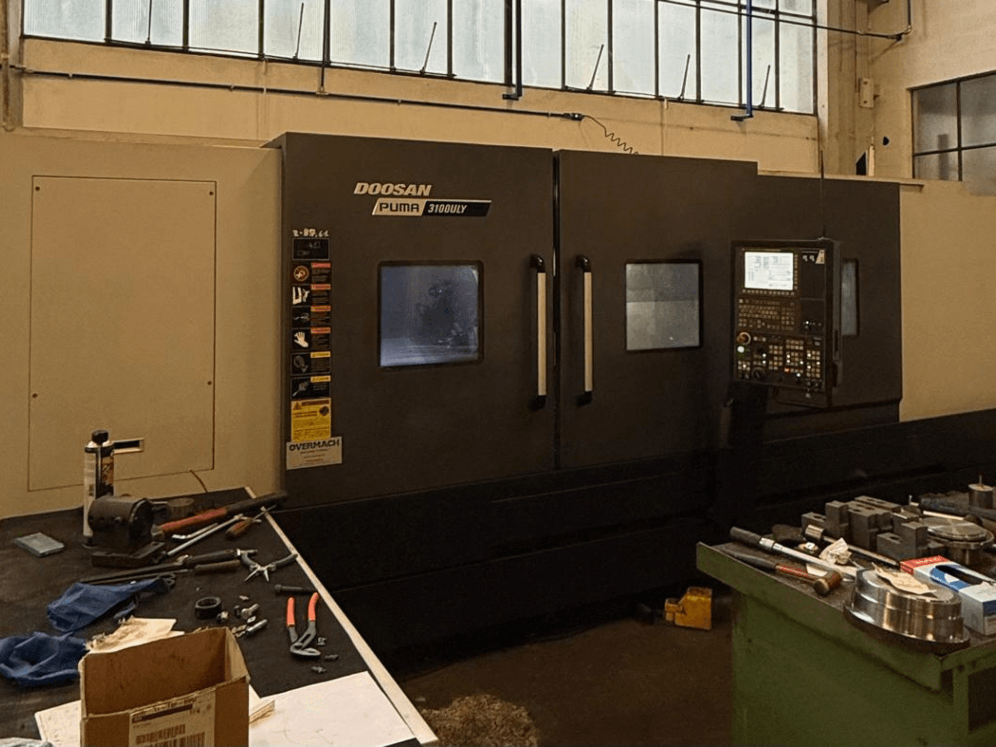 Tour CNC Doosan Puma 3100LY dans un atelier, vue latérale, avec le panneau de commande et les outils visibles sur l'établi.