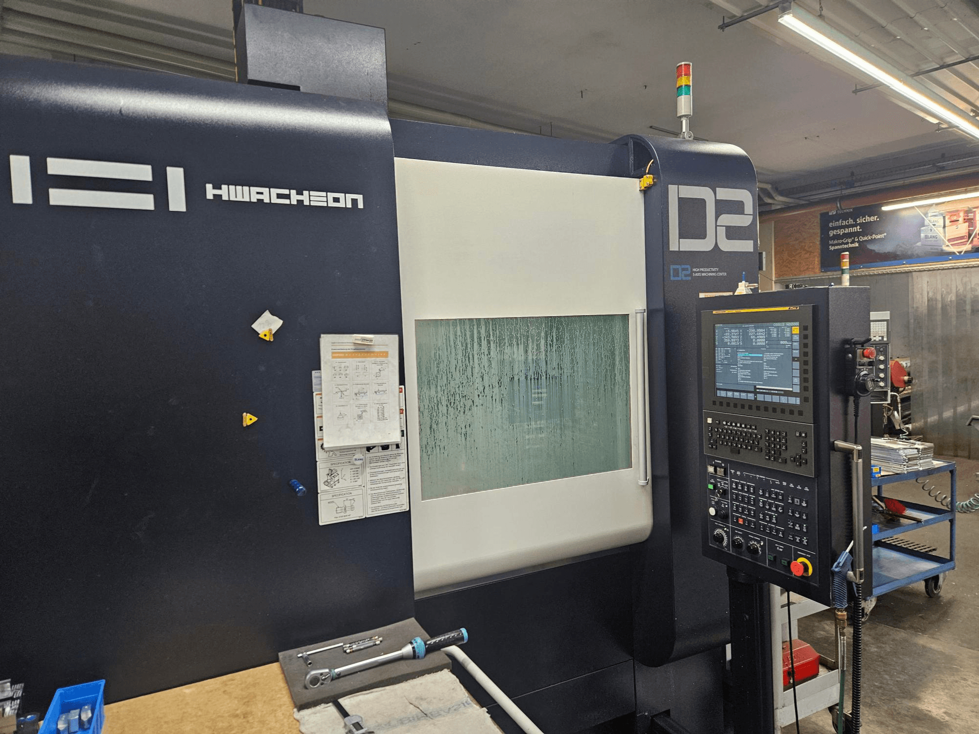Centre d'usinage vertical HWACHEON D2-5AX 12k, vue de face montrant le panneau de commande et la vitre de visualisation embuée.