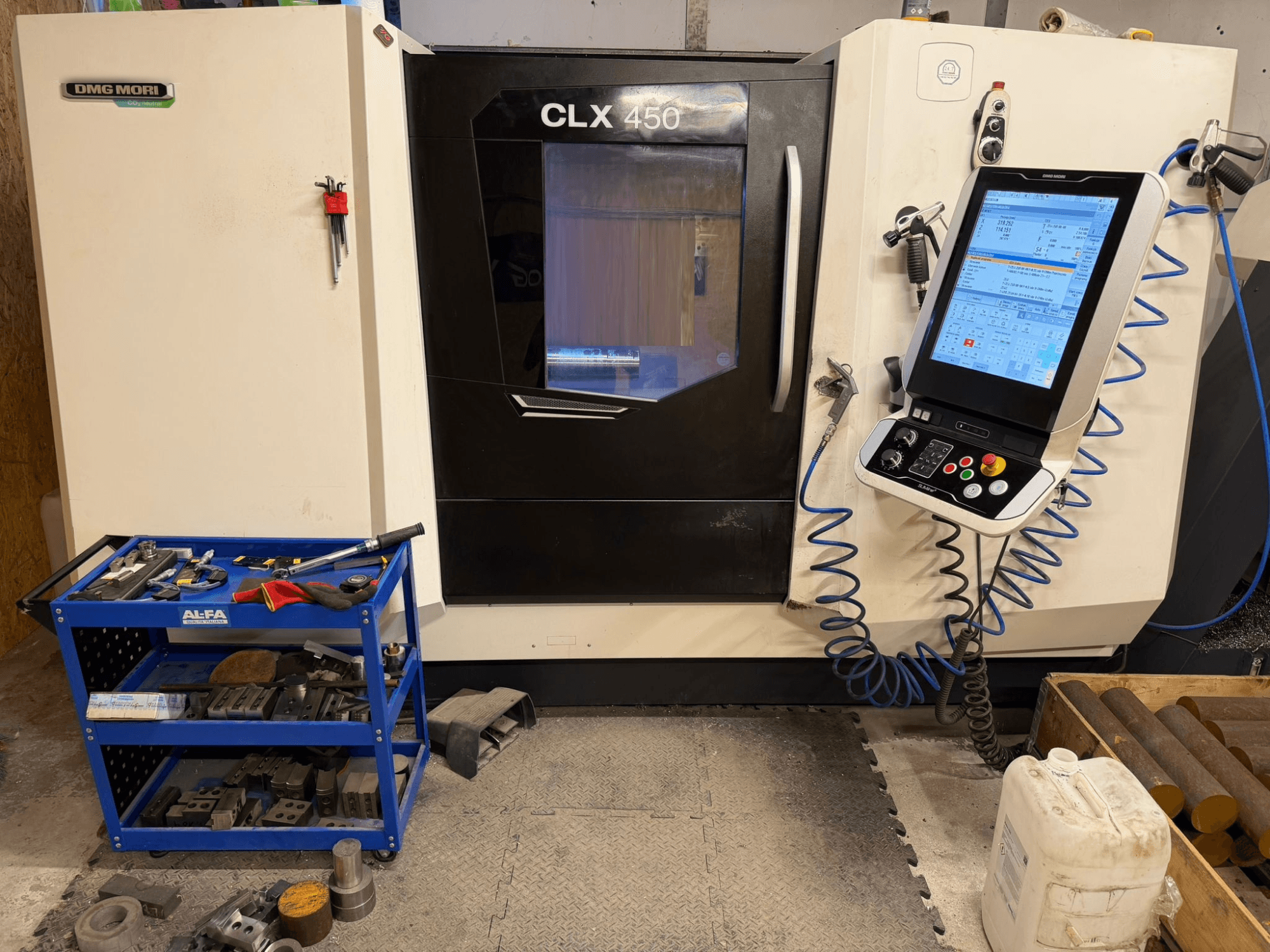 Vue de face du tour horizontal DMG MORI CLX 450 V3, avec un panneau de commande et un chariot d'outils à proximité avec des équipements.