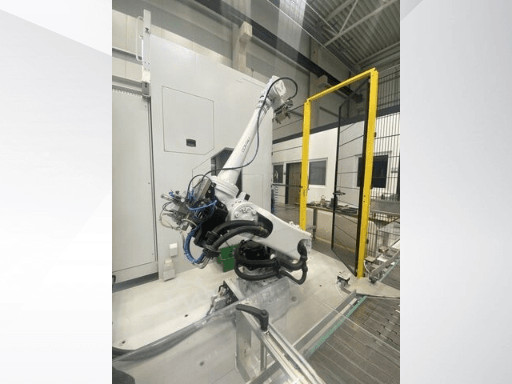 Bras robotique COMAU Smart NJ 40-2.5 en vue latérale, avec des câbles et une barrière de sécurité jaune dans un environnement d'usine.