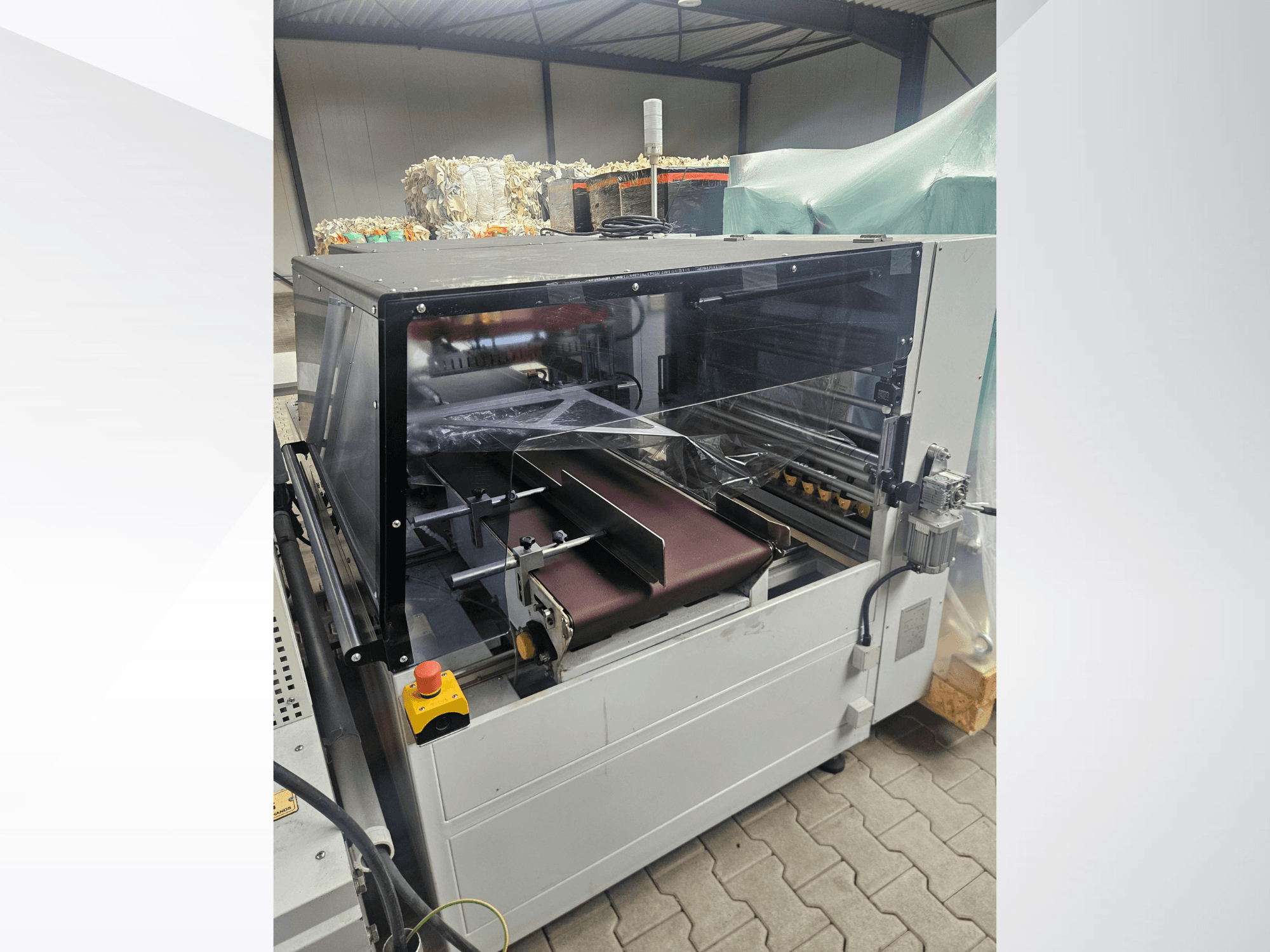 Machine AMTEC Speed Shrink 40 PRO, vue de face, présentant un mécanisme de transformation du plastique équipé d'un capot de sécurité transparent et d'un tapis roulant.