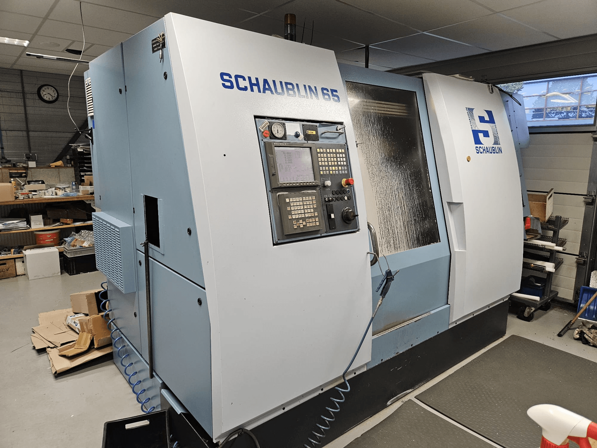 Machine CNC SCHAUBLIN 65, vue de côté, avec panneau de commande, boîtier bleu et gris et système de refroidissement visible.