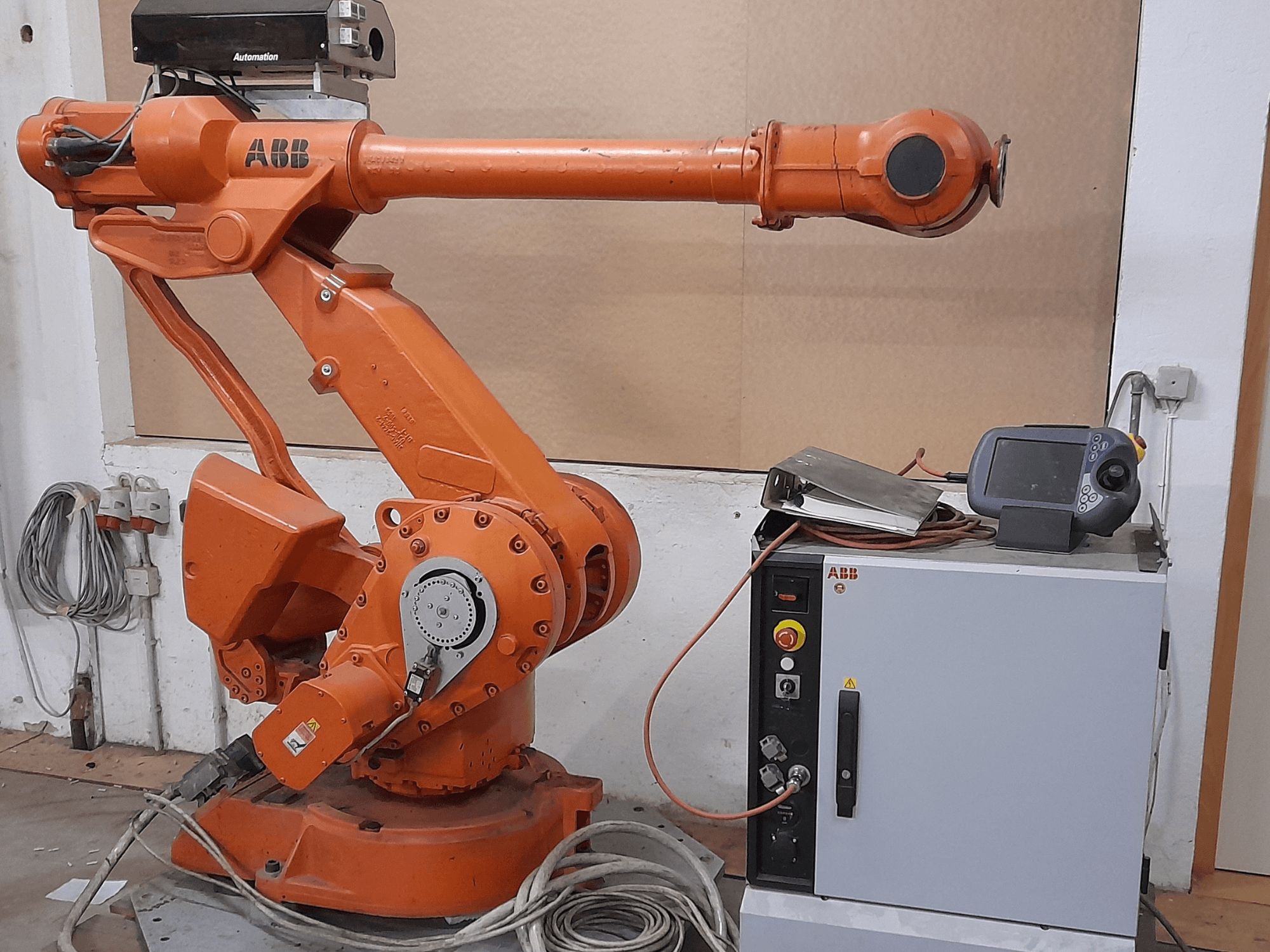 Bras robotique ABB orange avec panneau de commande, vue de face, présentant des câbles et des équipements d'automatisation.