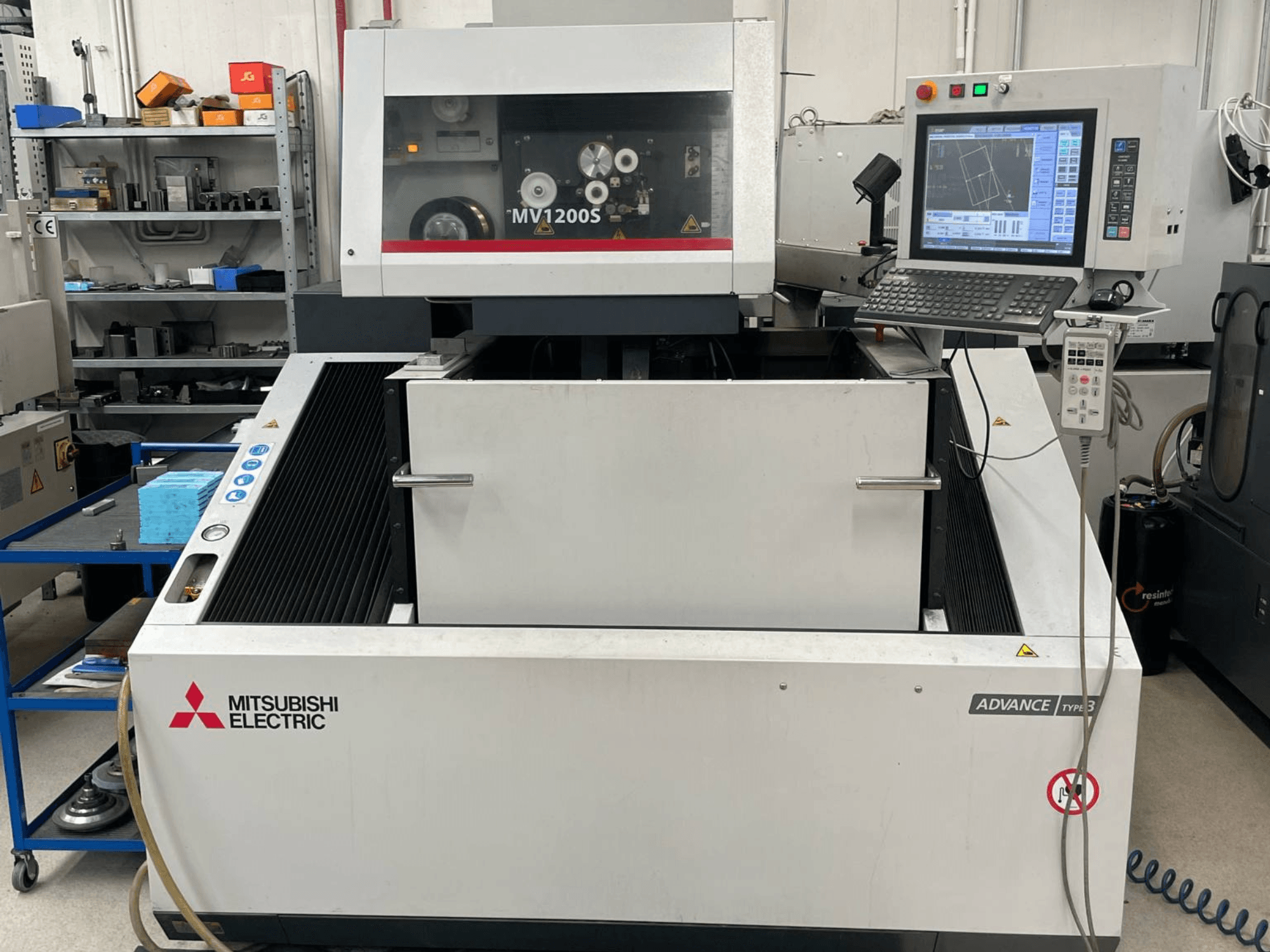 Machine d'électroérosion à fil Mitsubishi MV1200S vue de face, montrant le panneau de commande et la zone de travail, avec les avertissements de sécurité bien visibles.