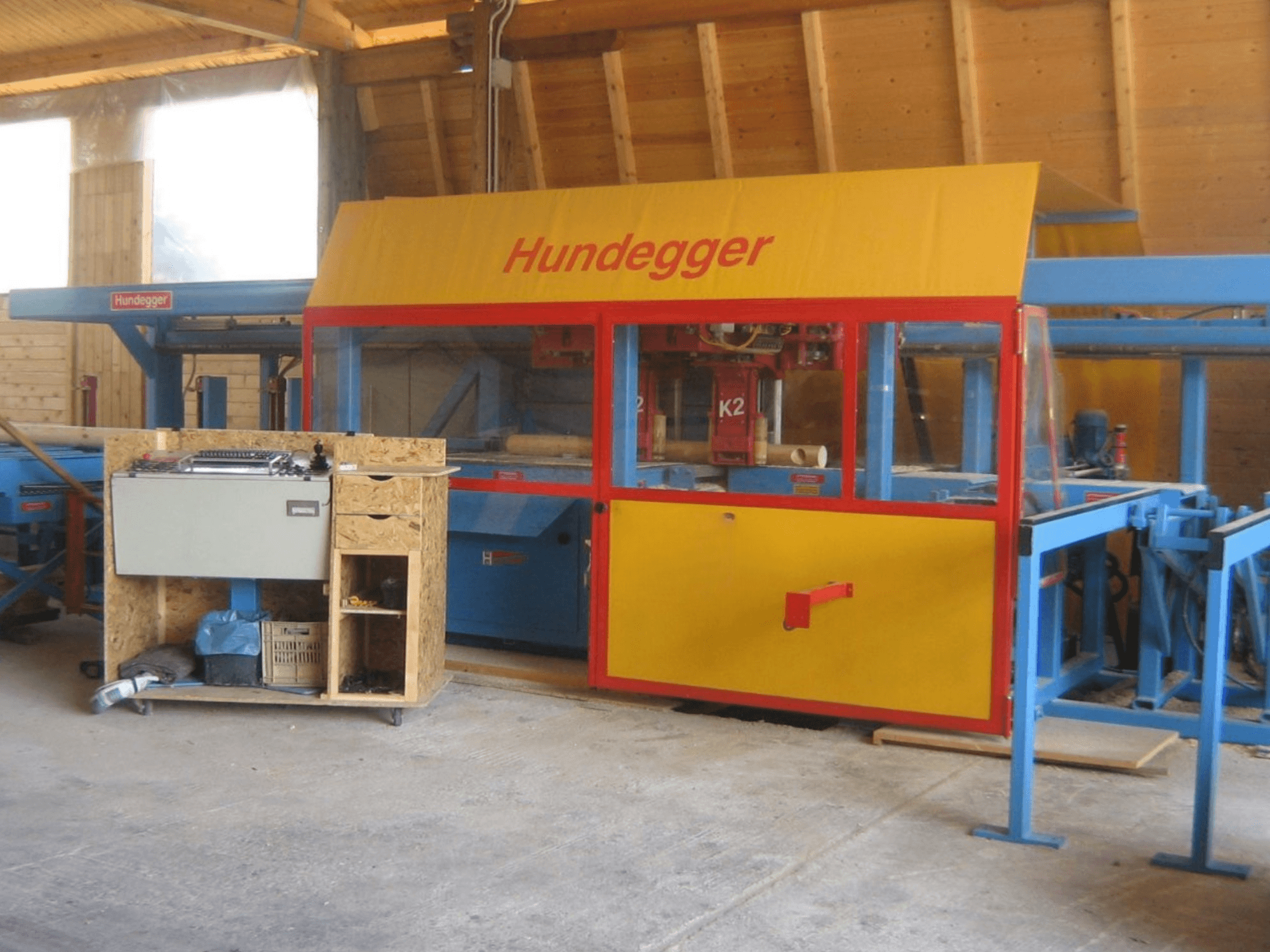 Centre d'usinage du bois CNC HUNDEGGER K2 4 assi dans un atelier, vue de face montrant le design jaune et bleu avec la table de travail.