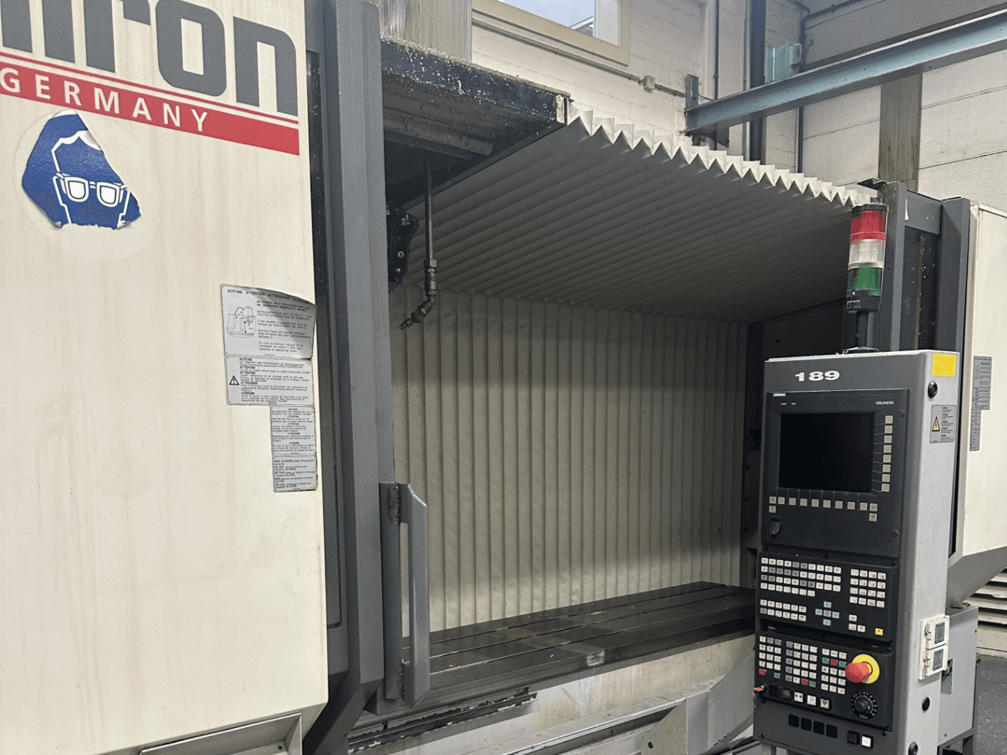 Alt text : Vue de face d'une machine CNC Hermle avec un panneau de commande comportant des boutons et un écran, avec une zone de travail ouverte.