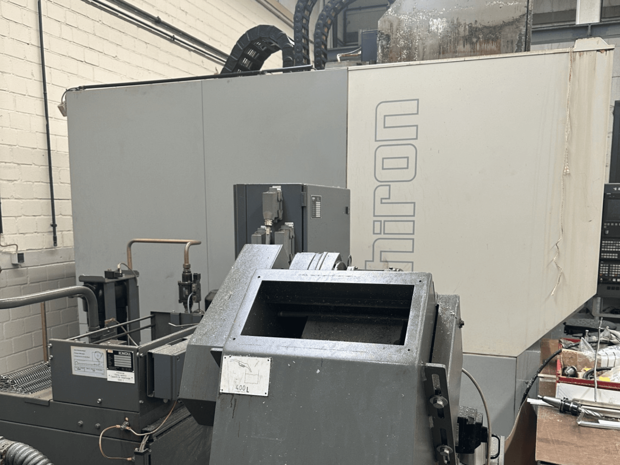 BRAND : Chiron ; Vue de face d'une machine industrielle à commande numérique avec l'extérieur gris, le panneau de commande visible et les composants de la machine au premier plan.