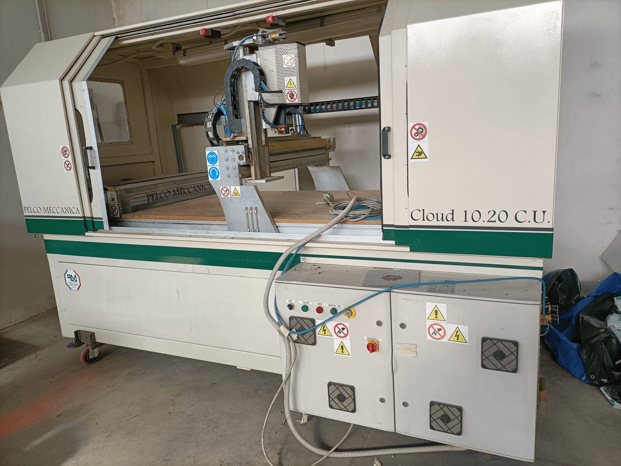 Défonceuse CNC MECCANICA CLOUD 10.20 C.U., vue de face montrant le panneau de commande et l'espace de travail, avec les étiquettes de sécurité et les tuyaux visibles.