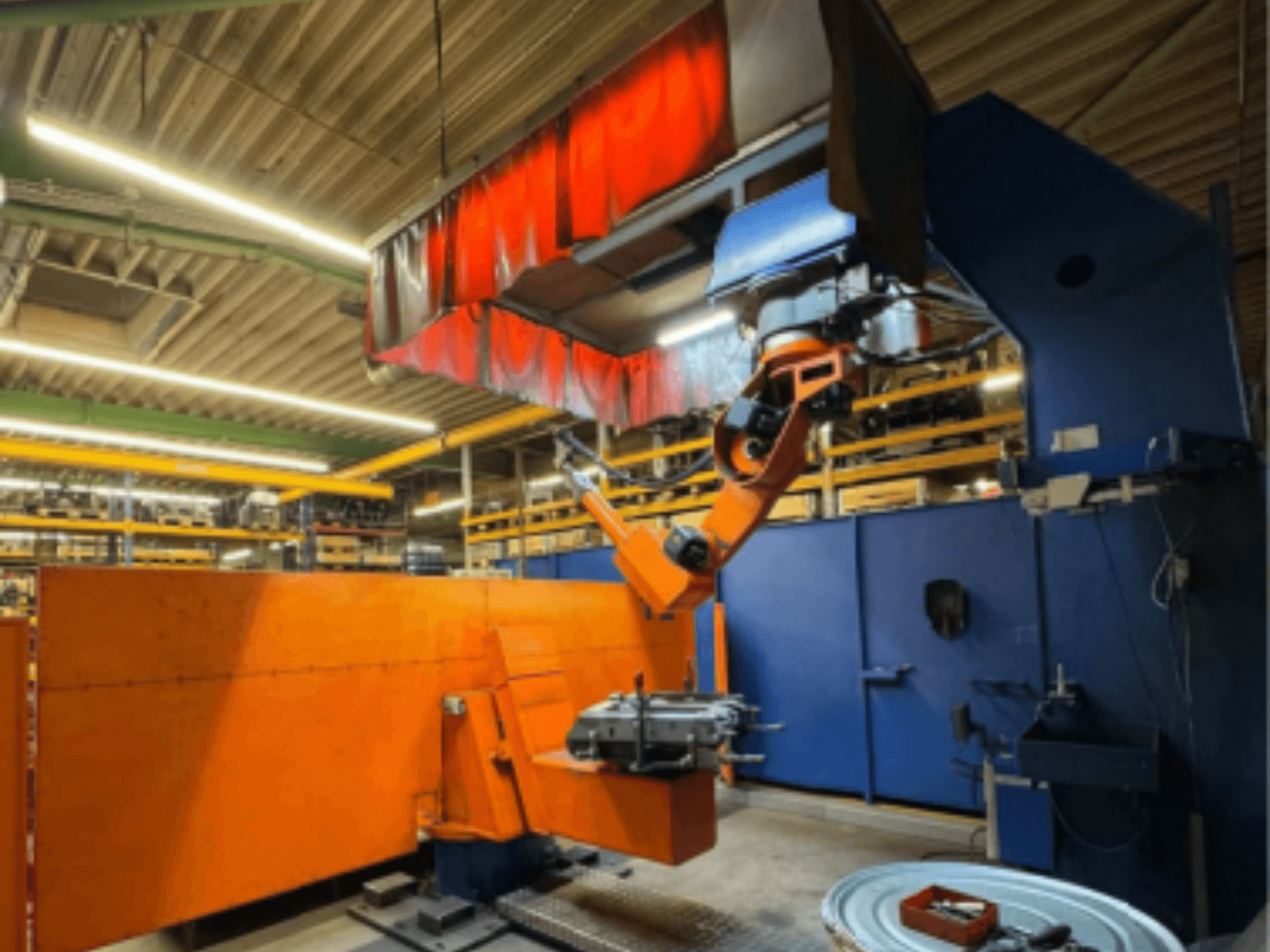 Robot soudeur CLOOS Romat 350 e en milieu industriel, vue de face avec le bras orange, tenant une pièce sous un rideau.