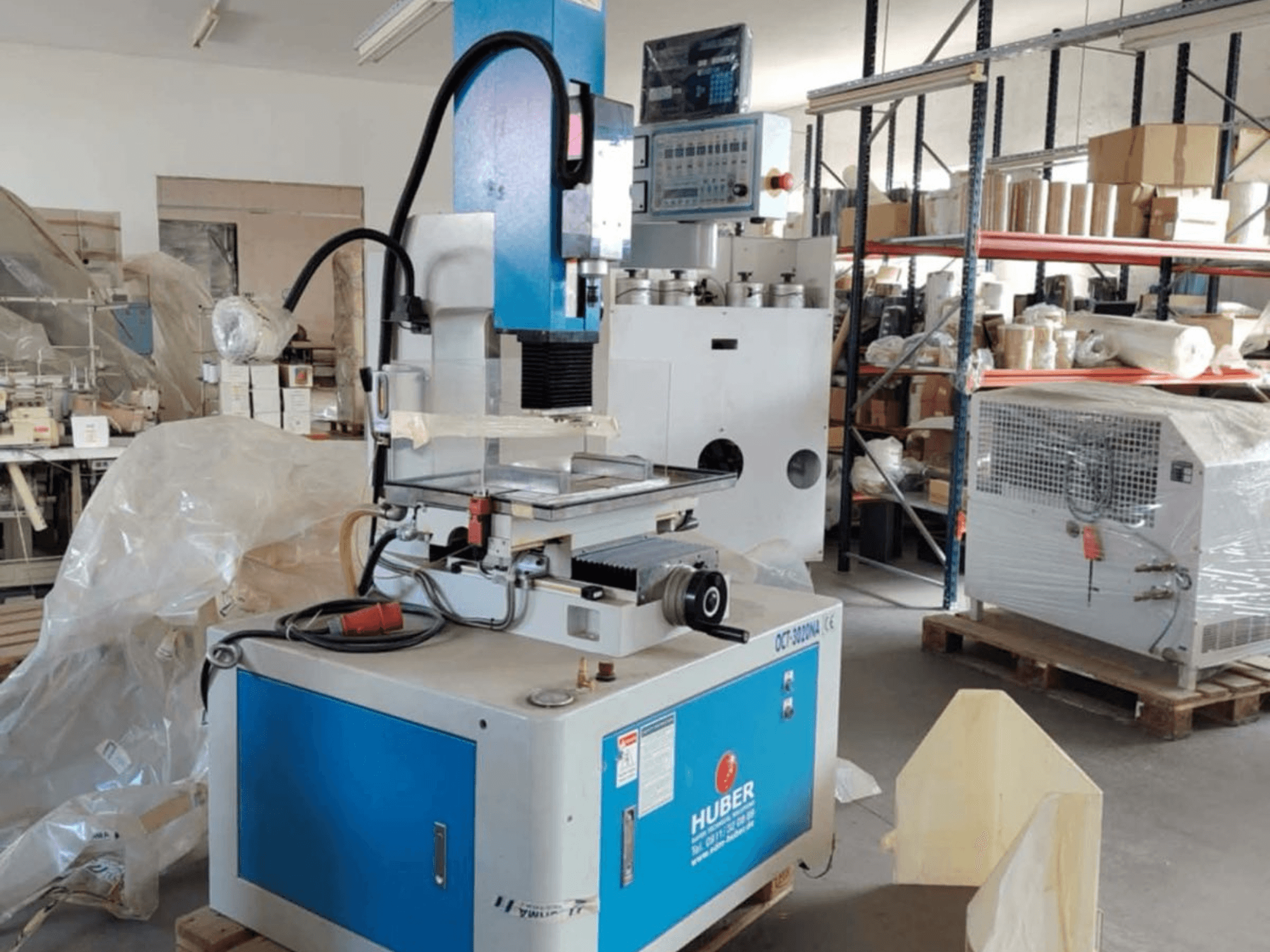 Machine d'électroérosion par enfonçage HUBER OCT-3020 NA dans un atelier, vue de face montrant le boîtier bleu et gris, les commandes numériques et la zone de travail.