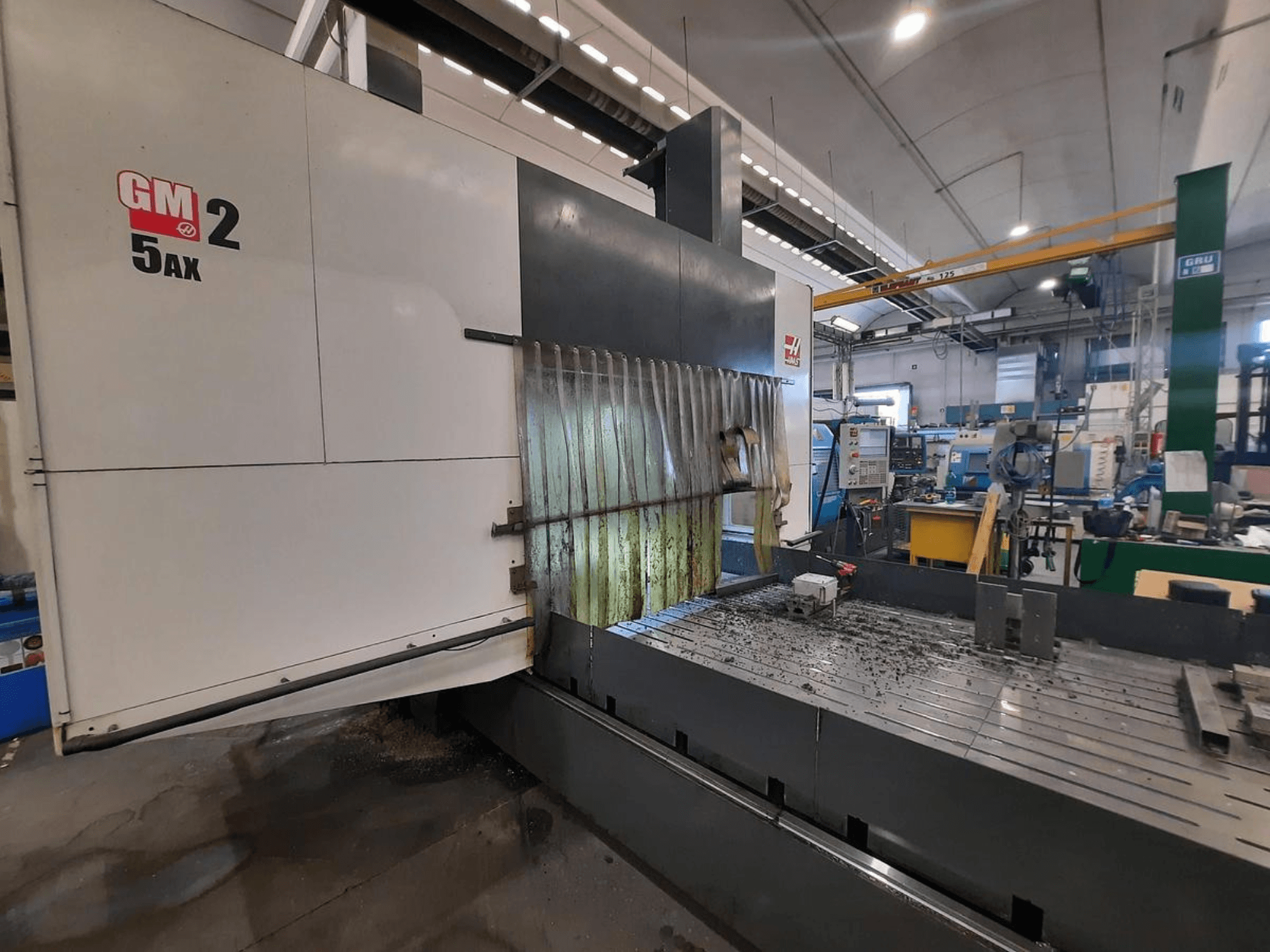 Machine CNC GM 2 5AX dans un atelier, vue latérale, montrant la zone de travail et les copeaux de métal sur la surface du banc.