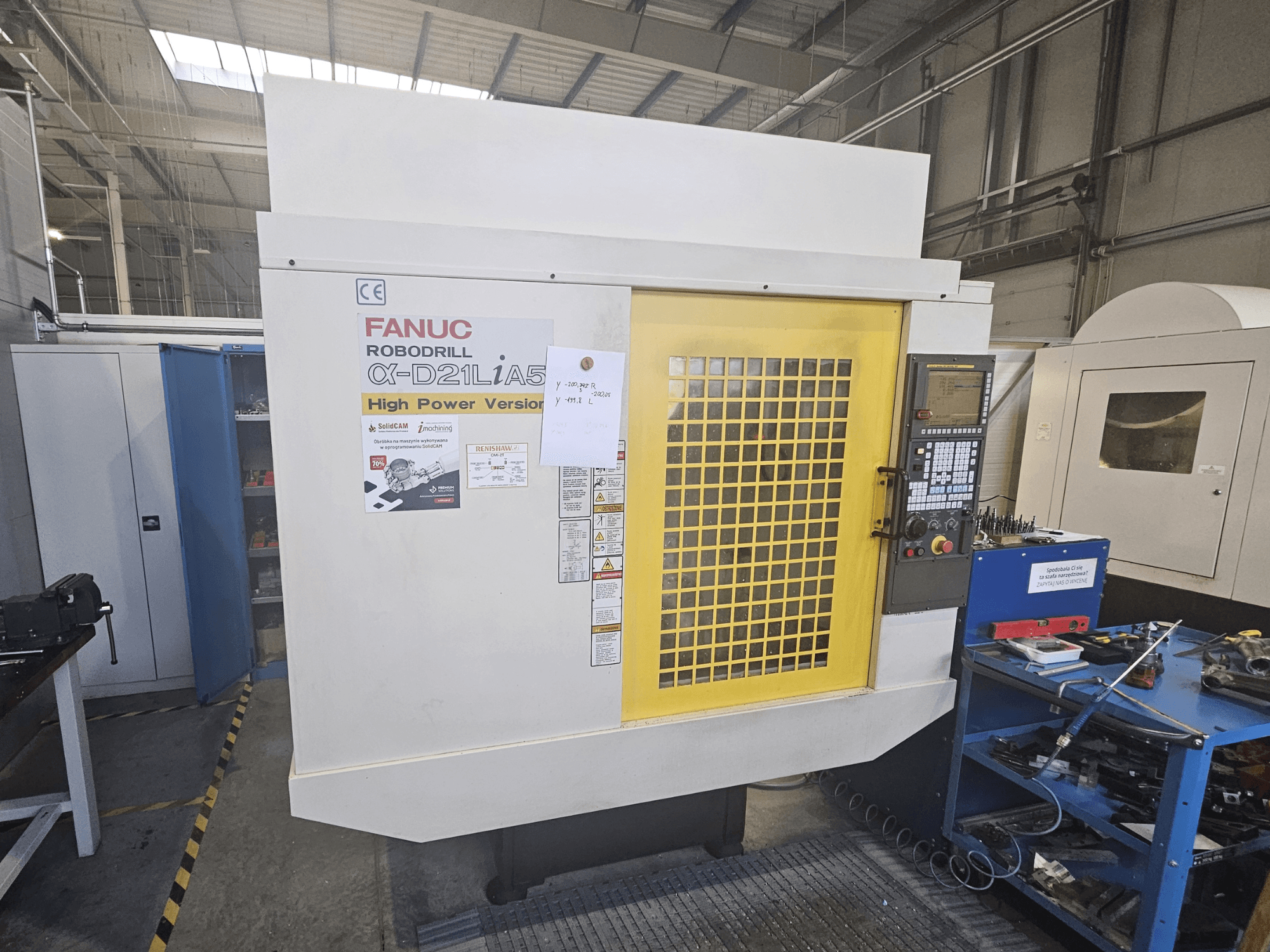Vue avant d'une FANUC Robodrill α-D21LiA5 avec la porte de sécurité jaune, le panneau de commande et les outils de l'espace de travail à proximité.