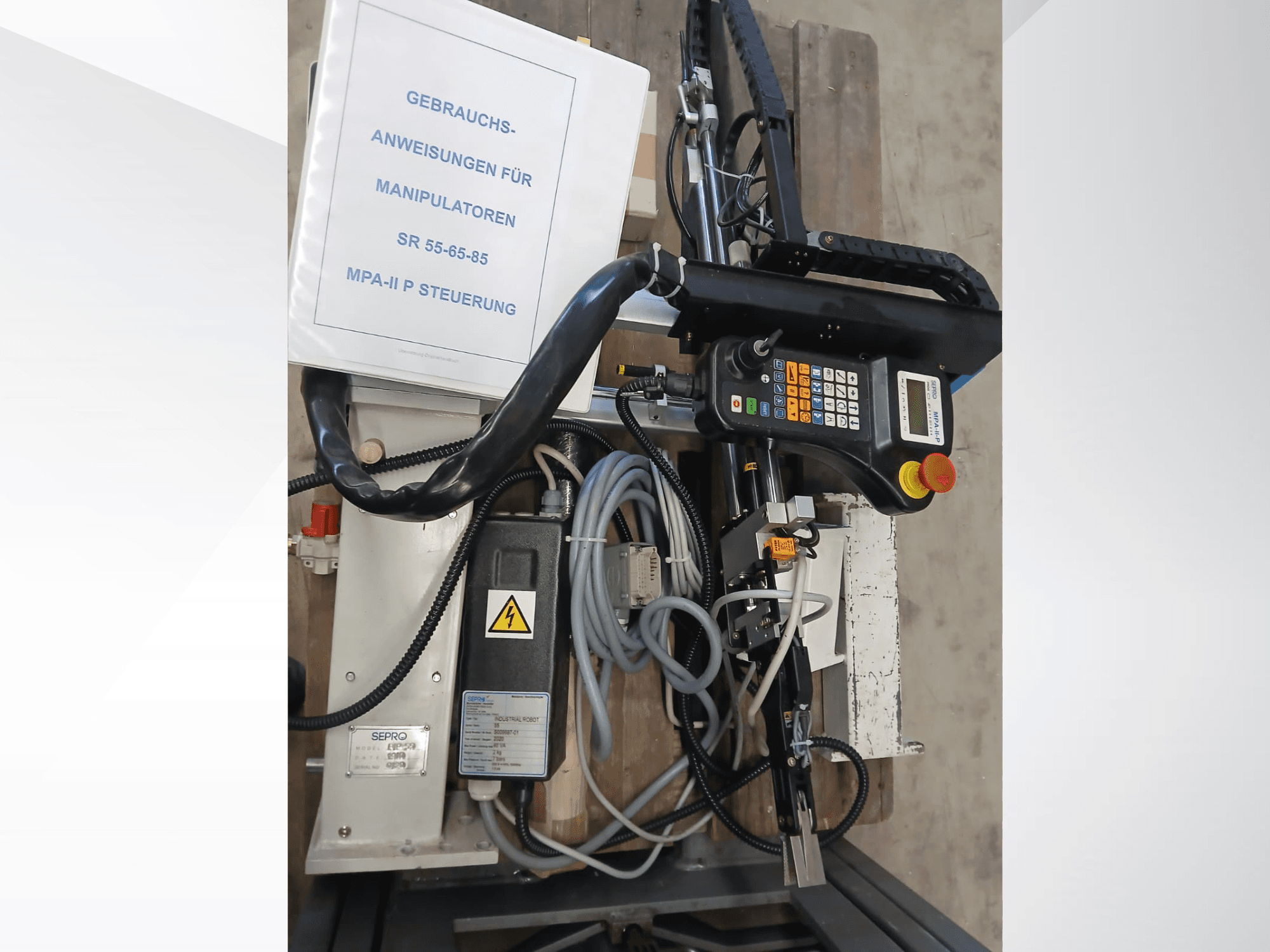 Panneau de commande et composants du robot portique Sepro PIP-55, vus de côté, avec le manuel d'utilisation visible.