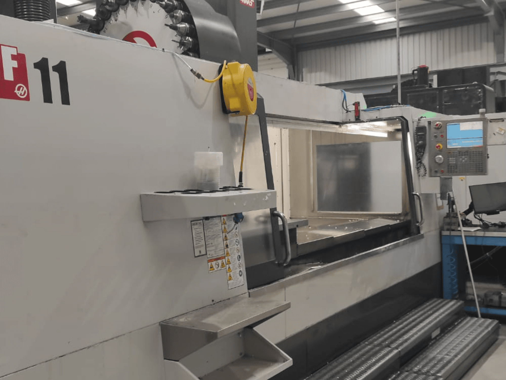 Machine Haas, modèle VF-11, présentée de face avec le panneau de commande, la grande zone de travail et les étiquettes de sécurité visibles.