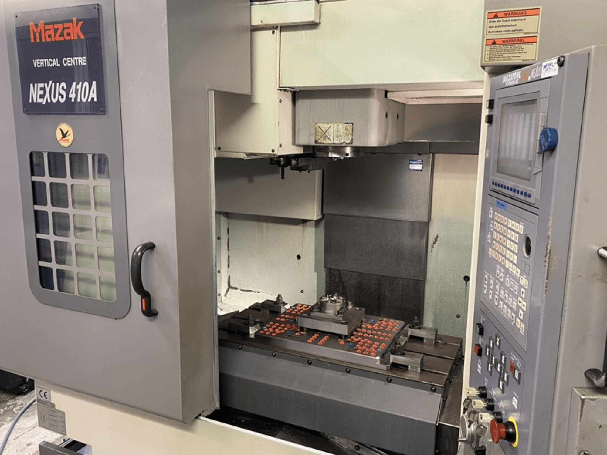 Centre d'usinage vertical Mazak VCN410, vue de face montrant le panneau de commande et l'intérieur de la machine avec la pièce à usiner montée.