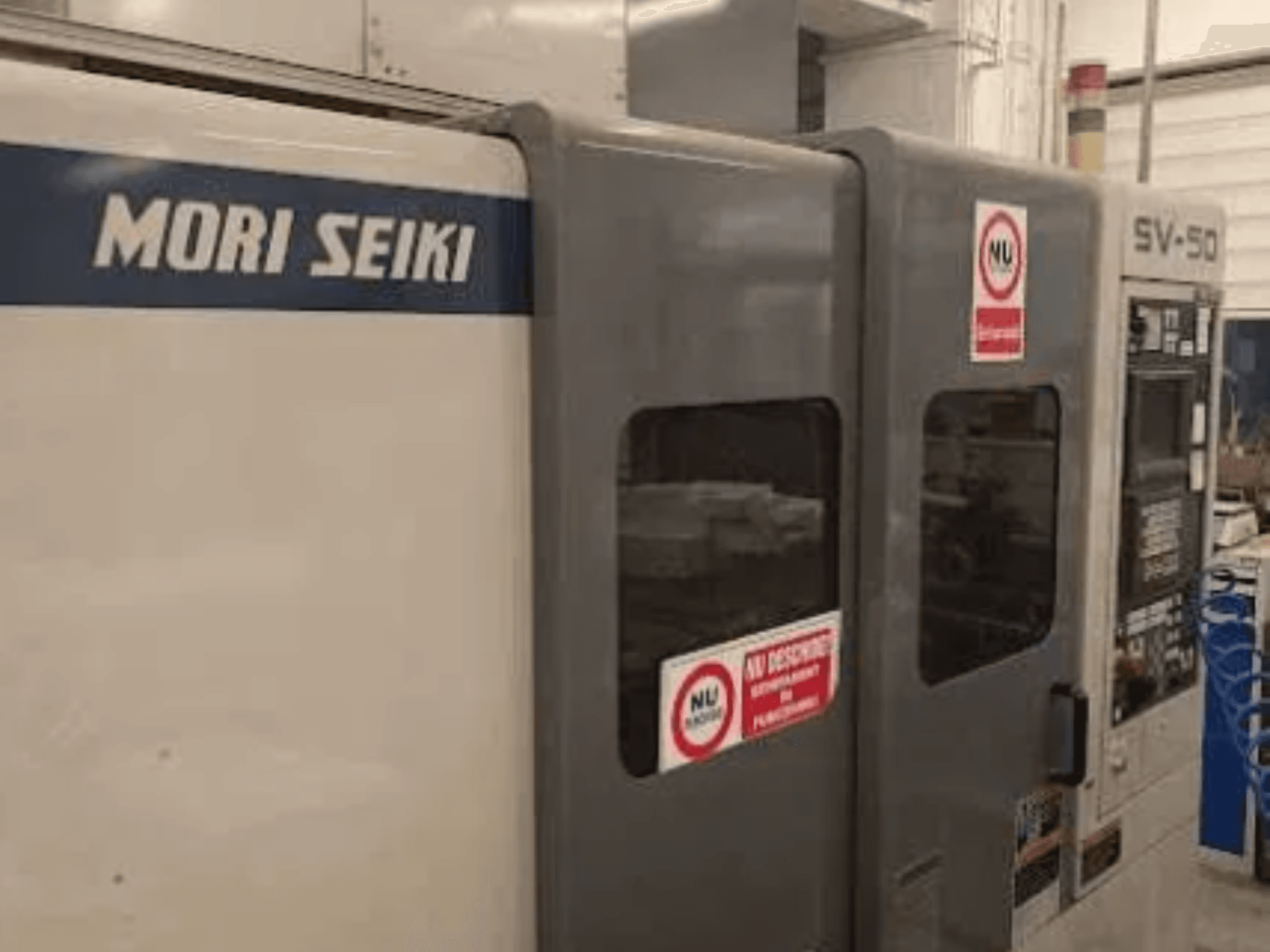 Machine CNC MORI SEIKI SV-50, vue de côté ; comprend le panneau de commande et les autocollants d'avertissement de sécurité.