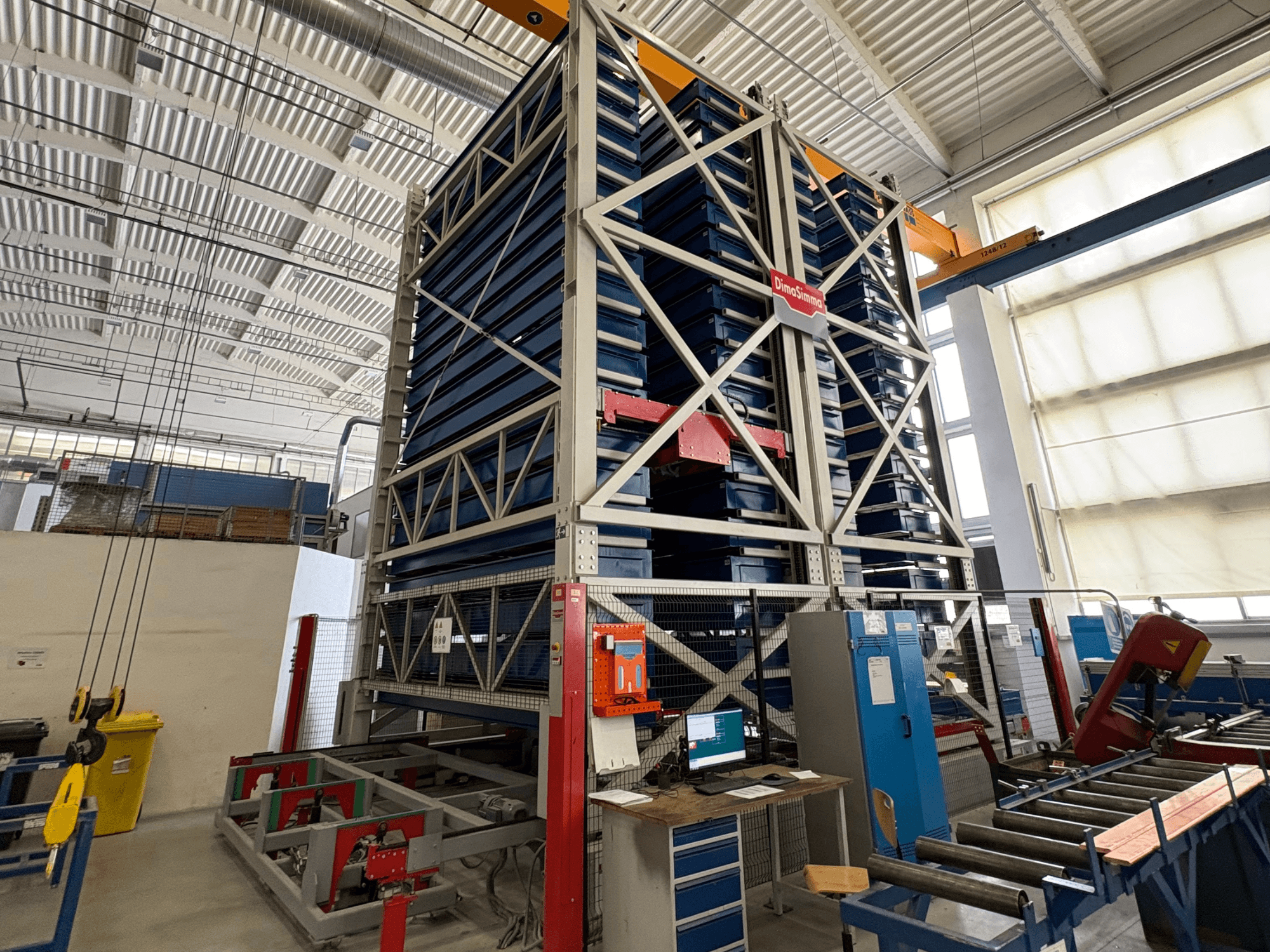 Machine à tôle DimaSimma EMS-30 TWIN dans un atelier, vue de face avec plateaux bleus empilés et poste de commande visible.