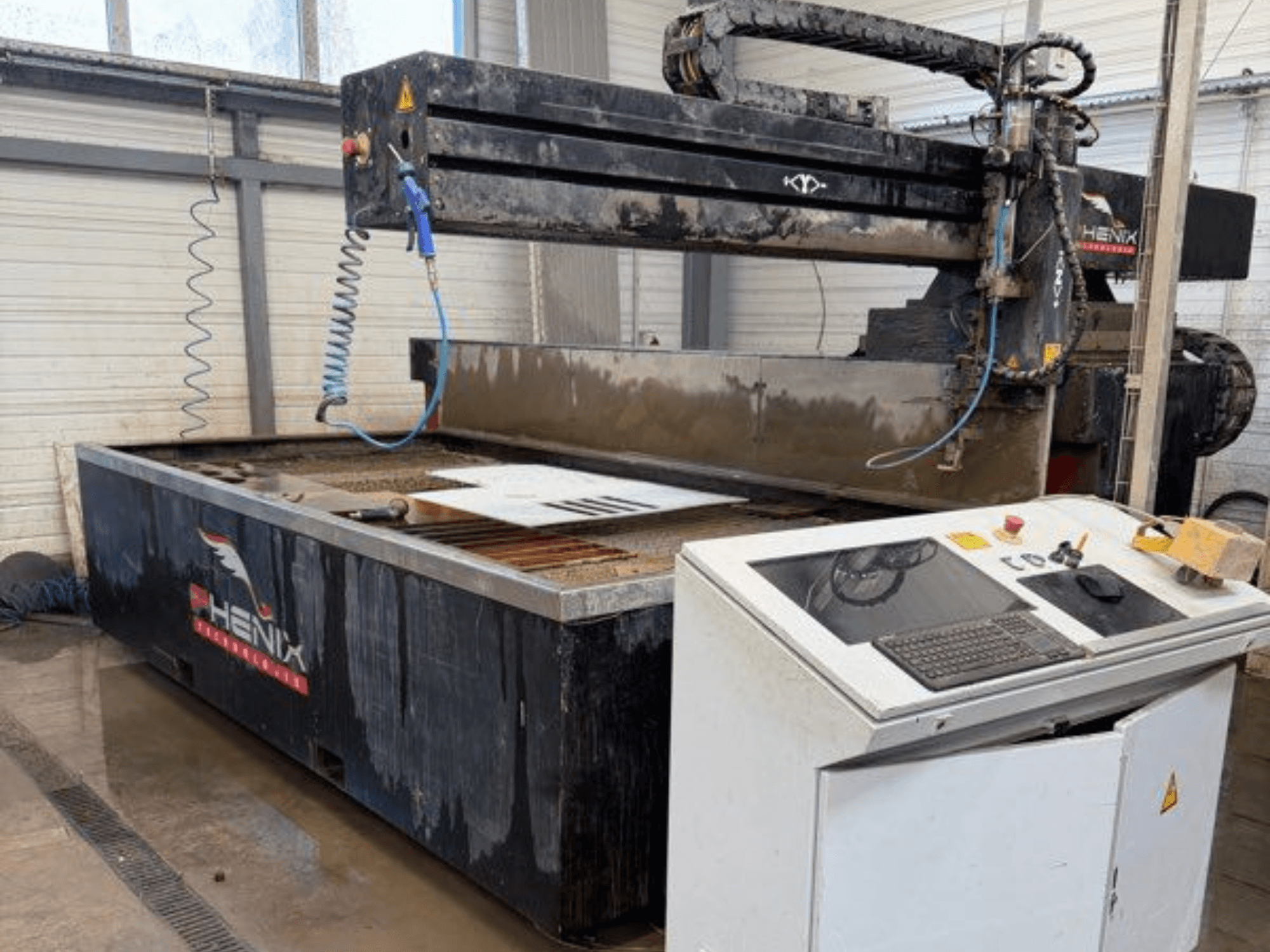 Machine de découpe au jet d'eau PHENIX MD JET 1530, vue de face montrant le panneau de commande et la zone de découpe avec le réservoir d'eau visible.