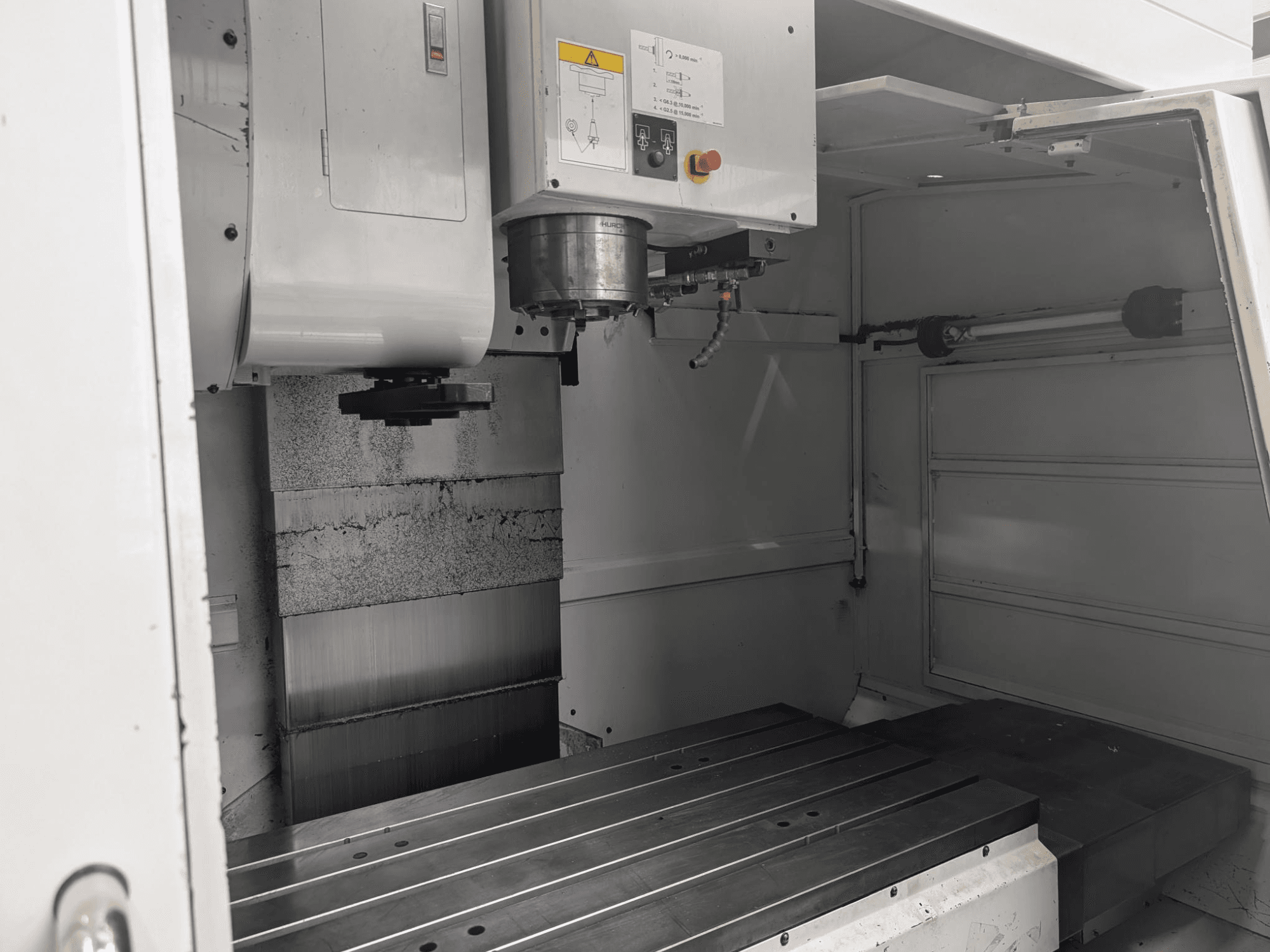 Vue intérieure d'une fraiseuse CNC avec une grande table de travail métallique et un moteur de broche, montrant les composants détaillés et le panneau de commande.