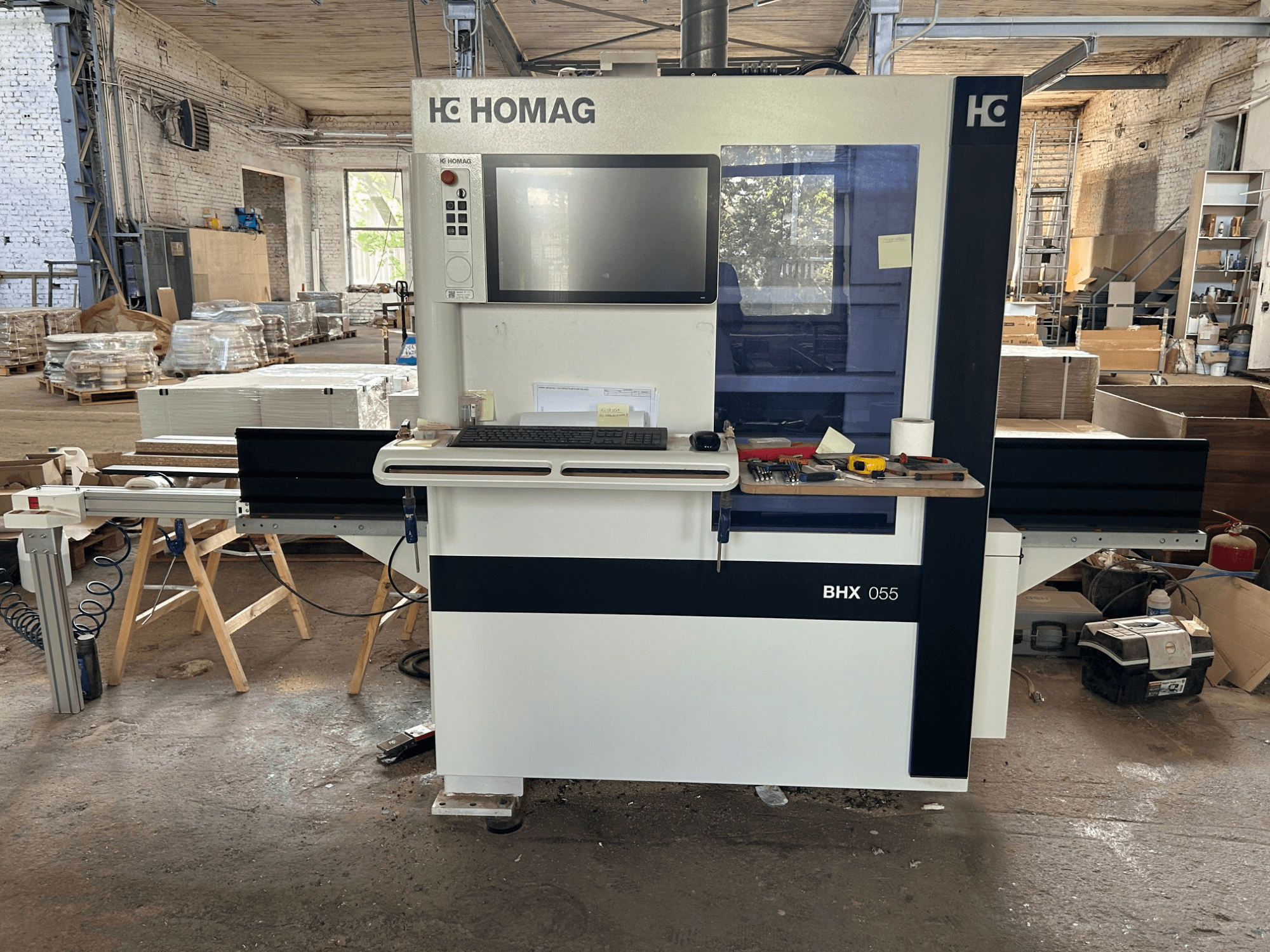 Centre d'usinage CNC HOMAG WEEKE OPTIMAT BHX 055, vue de face, montrant le panneau de commande et l'espace de travail avec les outils.