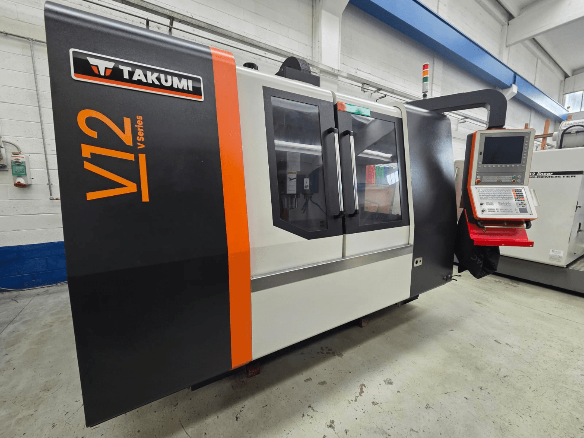 La fraiseuse CNC Takumi V12 série V, vue de face, comporte un panneau de commande et de grandes fenêtres en verre.