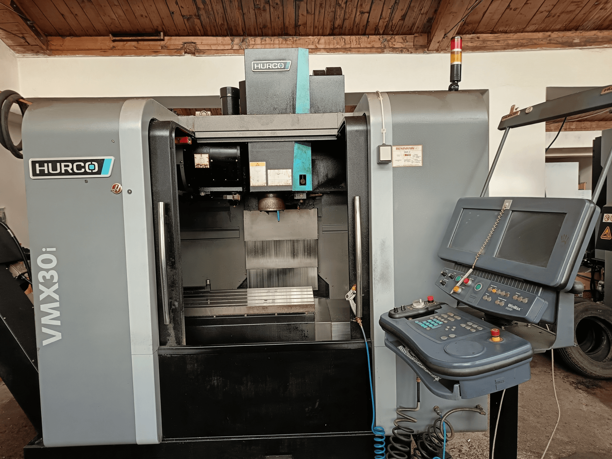 Centre d'usinage HURCO VMX30i en vue de face, avec panneau de commande avec boutons et écran, zone de travail métallique et voyant d'avertissement.