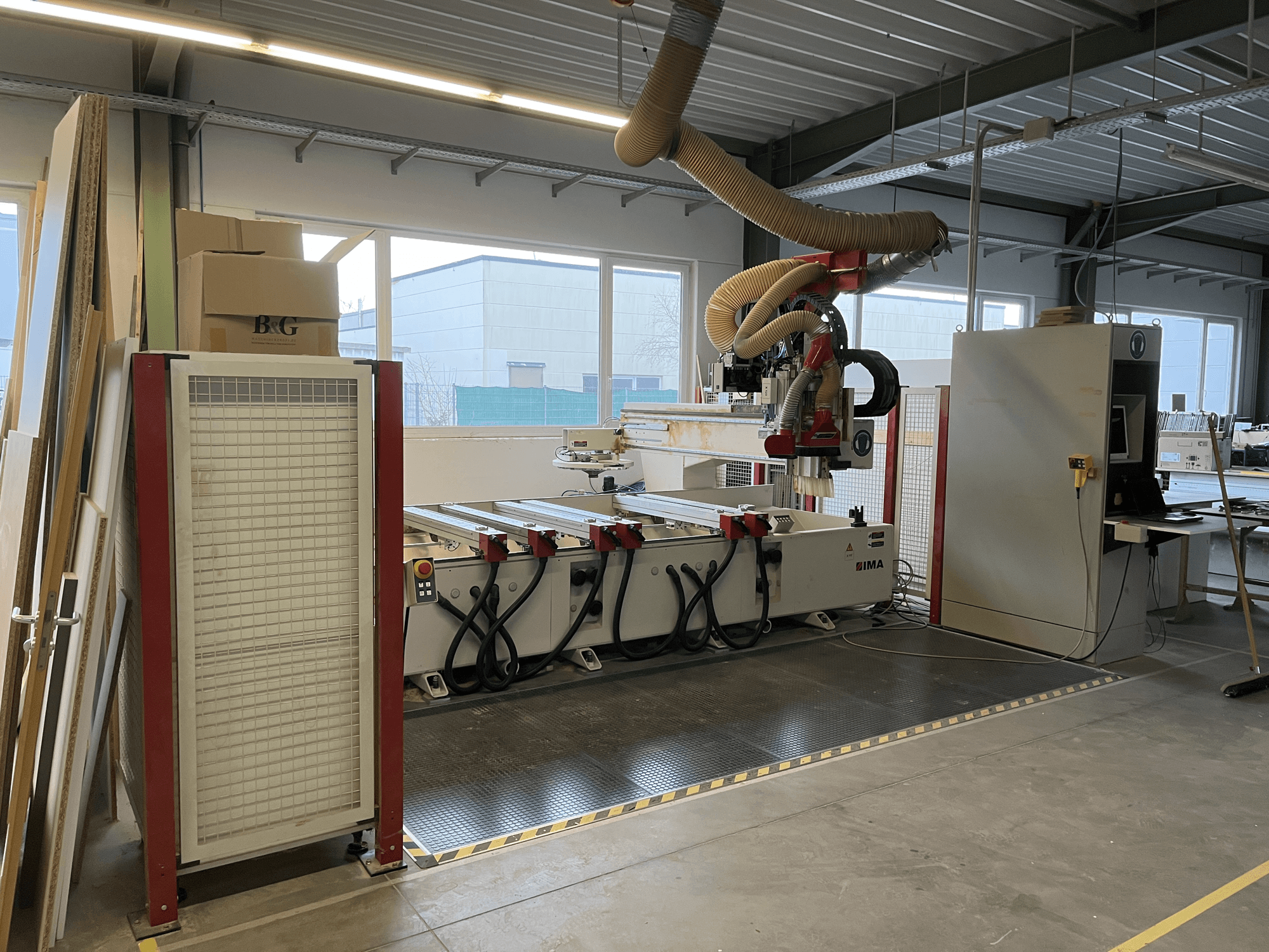 Centre d'usinage du bois CNC IMA BIMA 410 dans l'atelier, vue latérale avec panneau de commande et système d'extraction des poussières visibles.