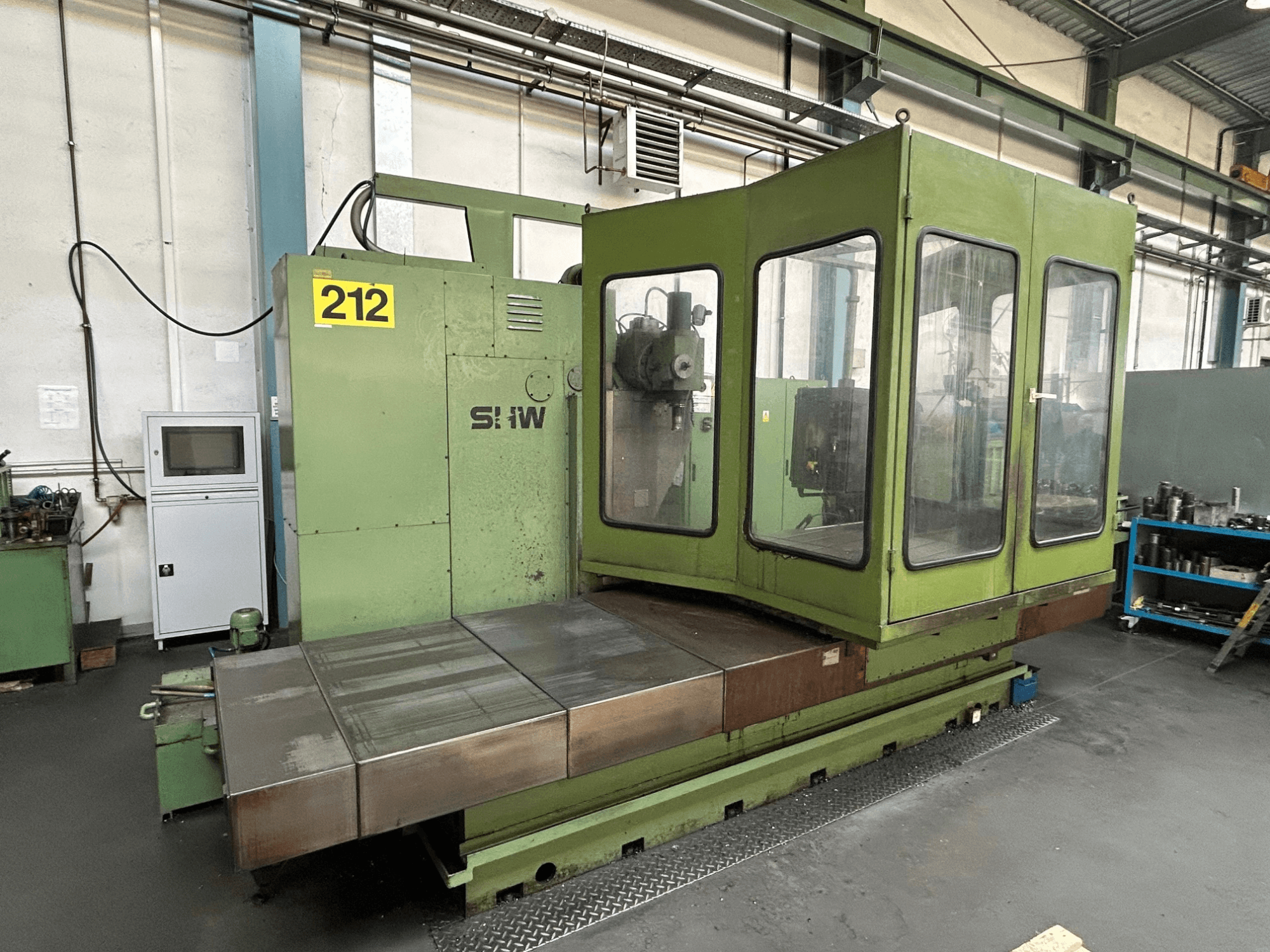 Centre d'usinage vertical SHW UF-5 en vert, vue de face montrant le panneau de commande, le boîtier en verre et la table de travail en métal.