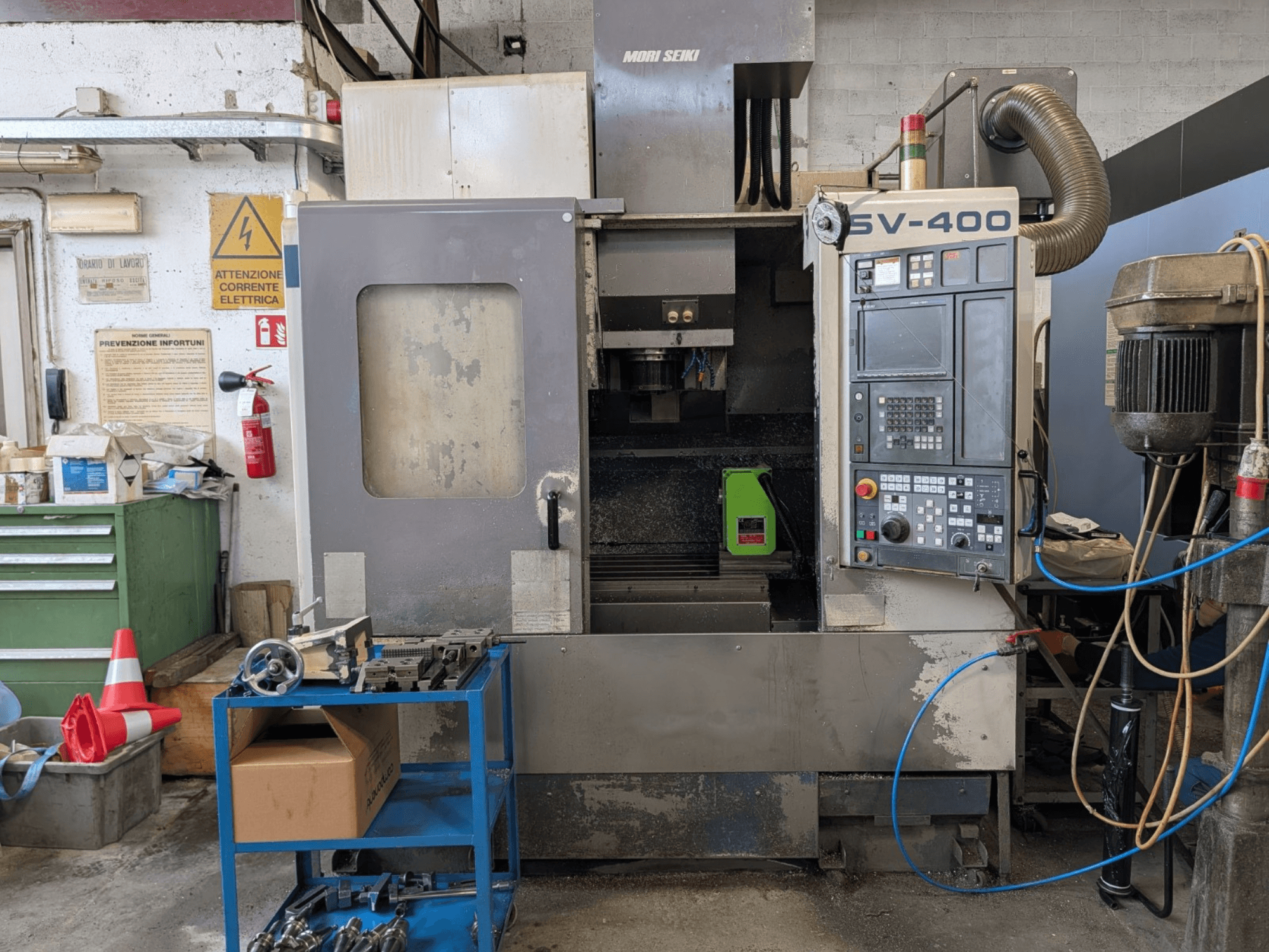Centre d'usinage vertical MORI SEIKI SV-400 dans un atelier, vue latérale, montrant le panneau de commande et les machines-outils à proximité.