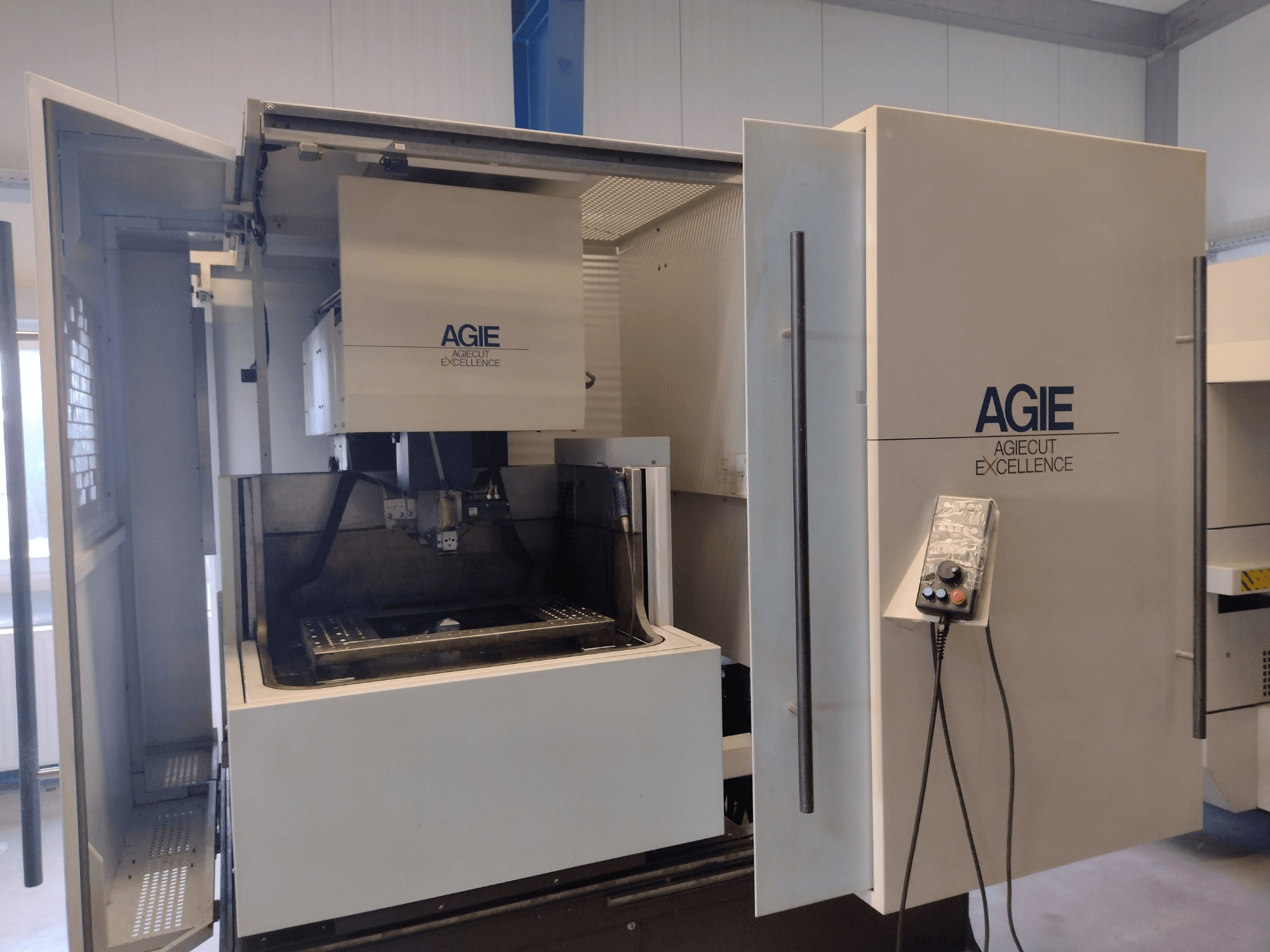 Vue de face d'une machine d'électroérosion à fil AGIE Progress 3, présentant une armoire ouverte, un panneau de commande et une zone d'usinage.