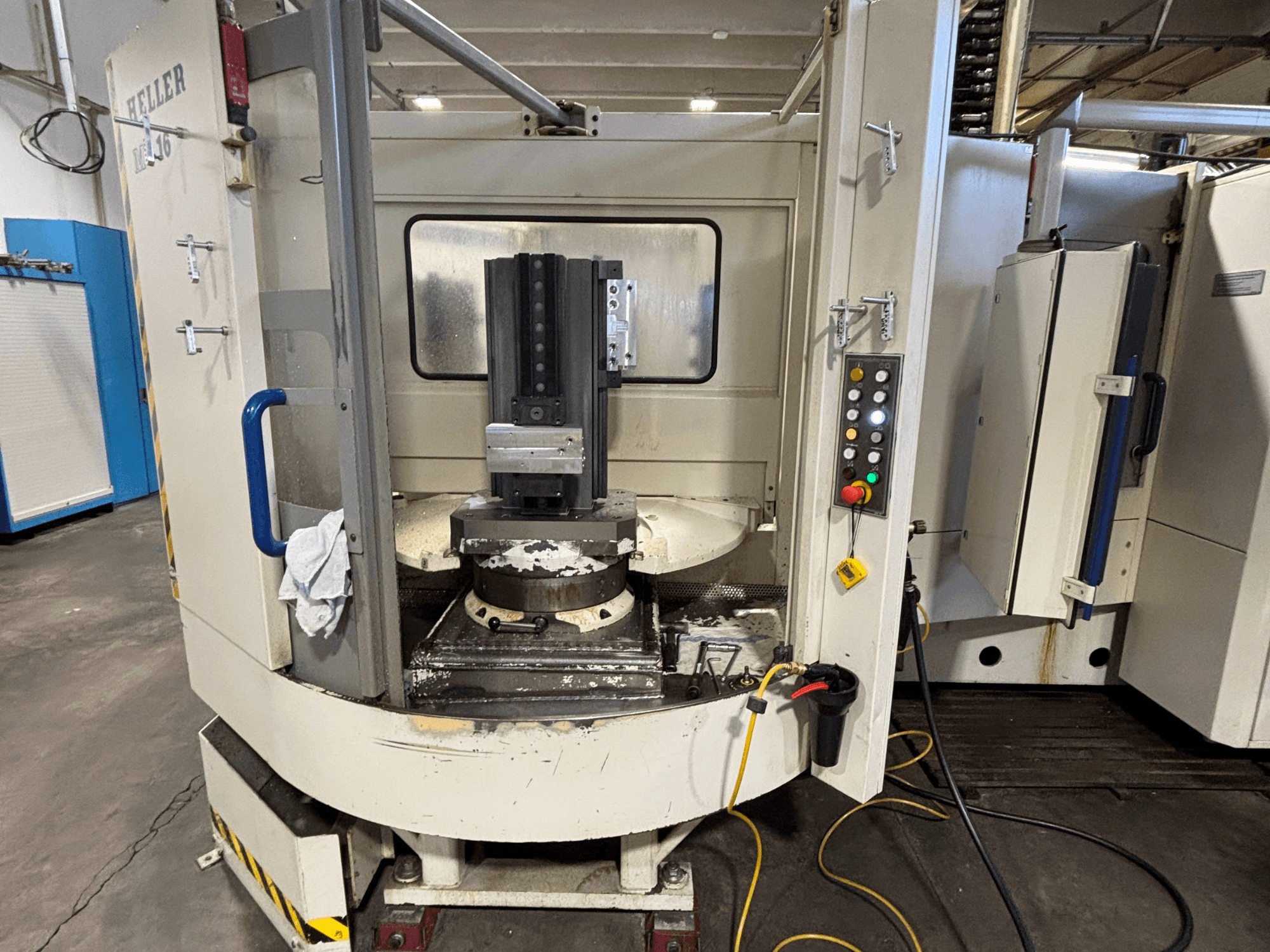 Centre d'usinage Heller, modèle vertical, vue de face montrant la broche, le panneau de commande et la table de travail avec l'équipement fixé.