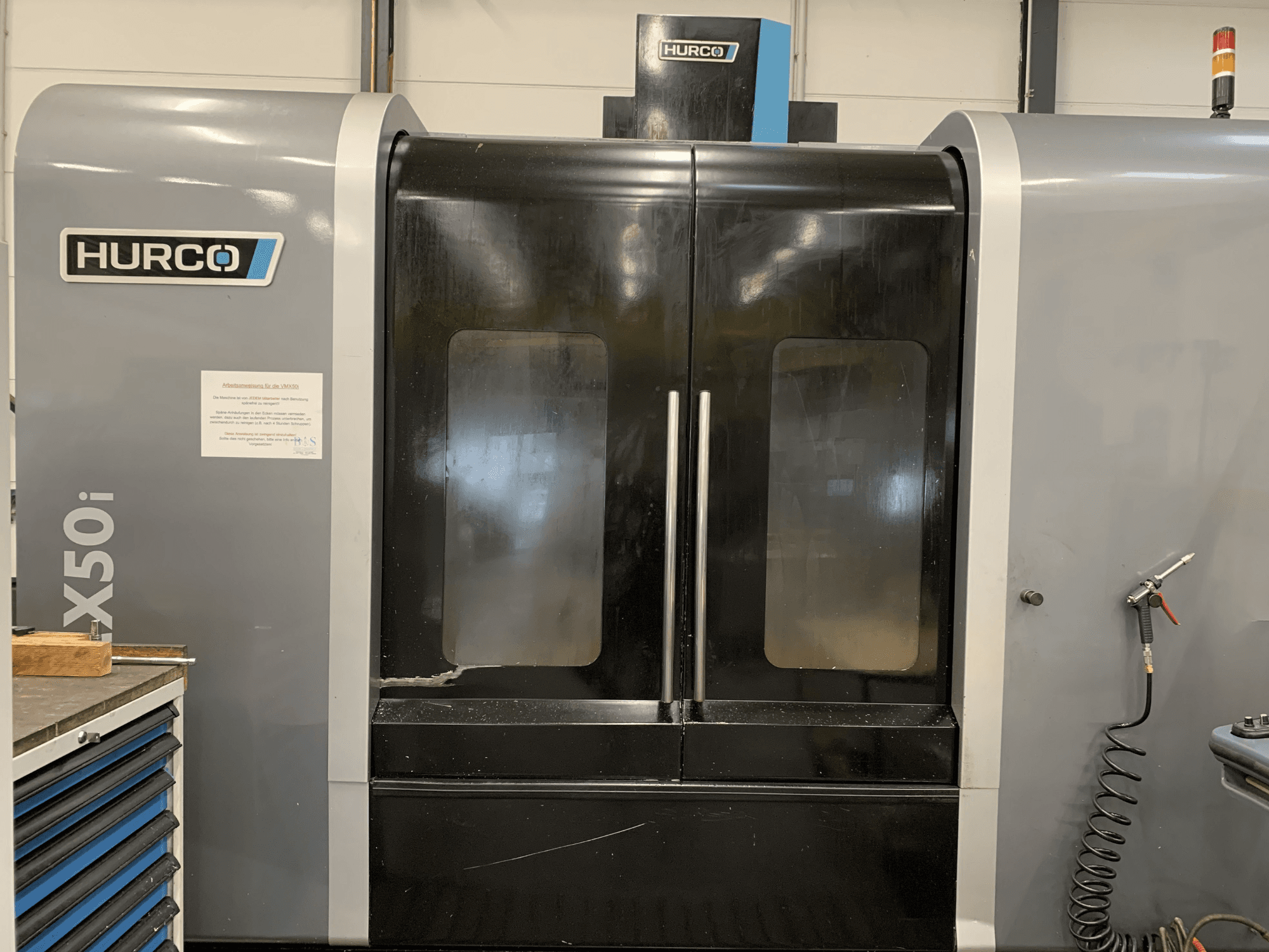 Vue de face d'une machine CNC Hurco VX50i avec deux portes, montrant les commandes techniques et un panneau de maintenance sur le côté.