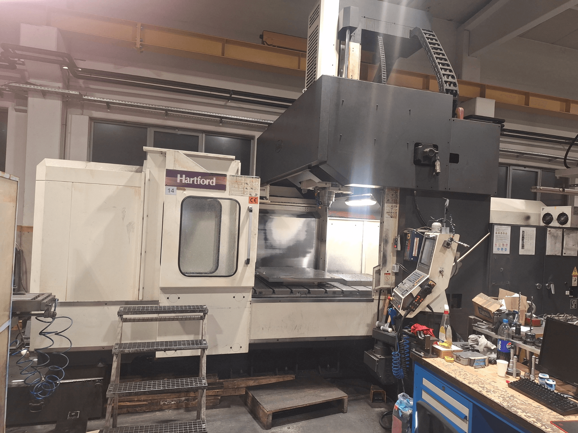 Machine CNC Hartford, vue de face, avec commandes techniques, marches d'accès et table de travail, dans un atelier.