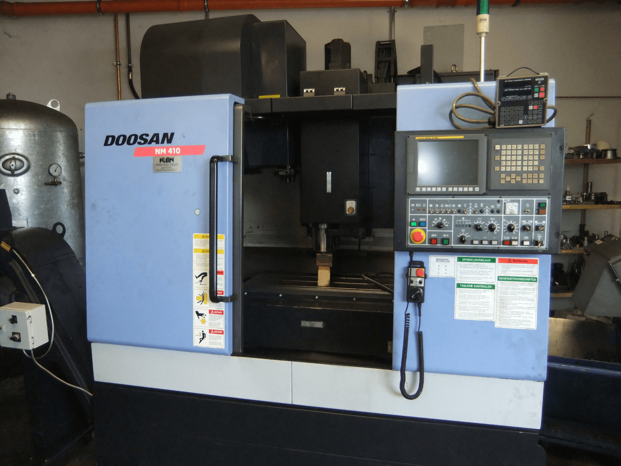 Centre d'usinage vertical DOOSAN NM 410, vue de face, montrant le panneau de commande, la zone de la broche et les étiquettes de sécurité.