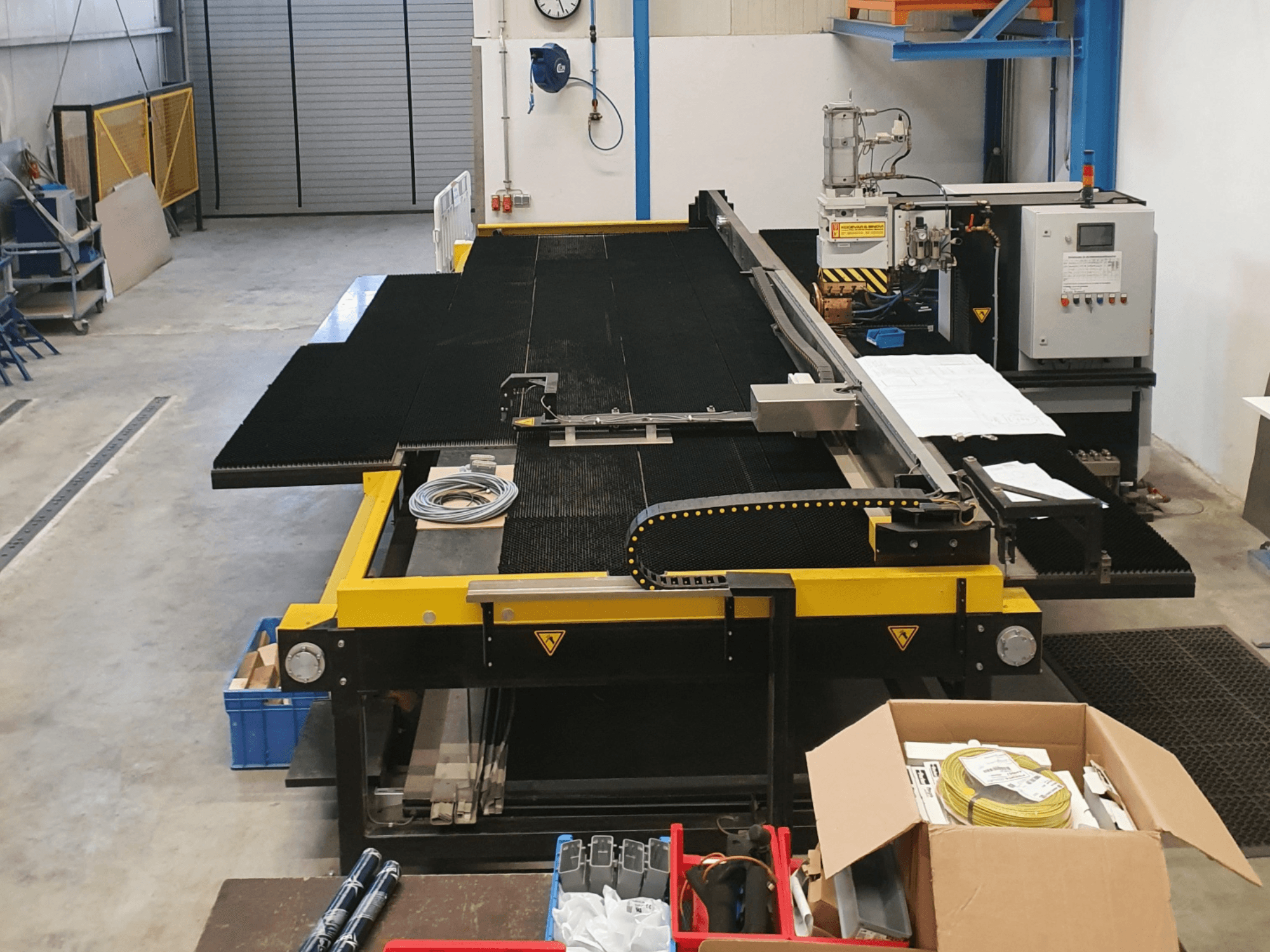 Machine à découper industrielle avec des caractéristiques jaunes et noires, vue de face, montrant les commandes et les accessoires dans un environnement d'usine.