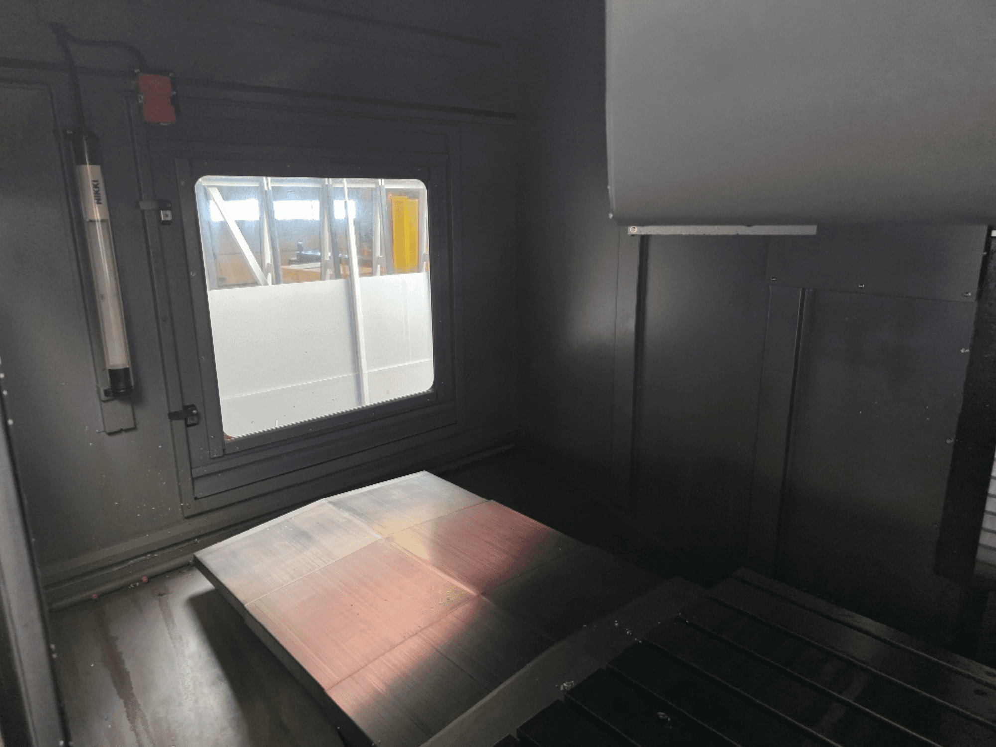 Vue intérieure d'un boîtier de machine avec une plaque de métal poli, une fenêtre latérale et un éclairage minimal. Aucune marque n'est visible.