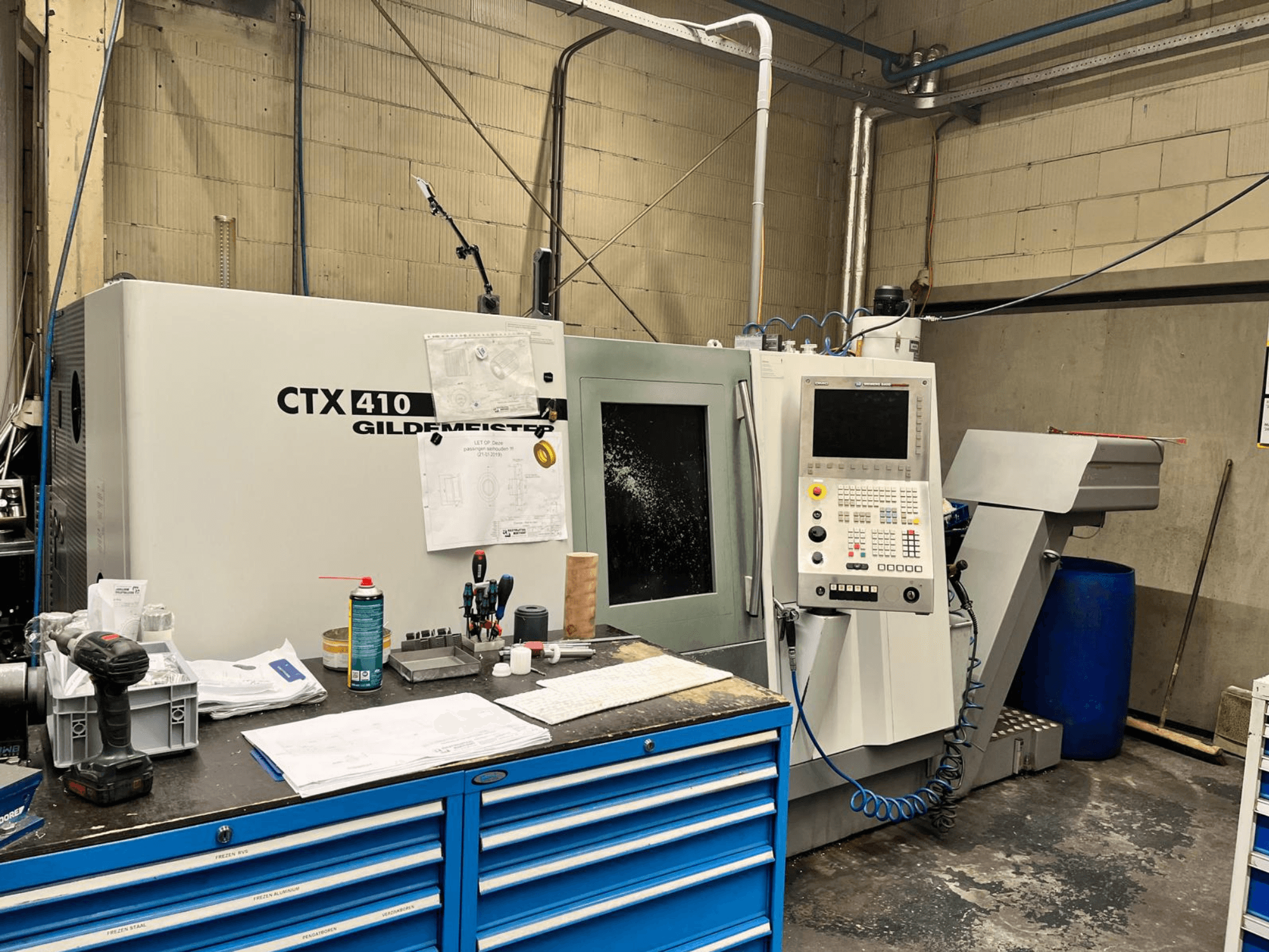 Machine CNC Gildemeister CTX 410 dans un atelier, vue de face, avec un panneau de commande et divers outils sur un établi.