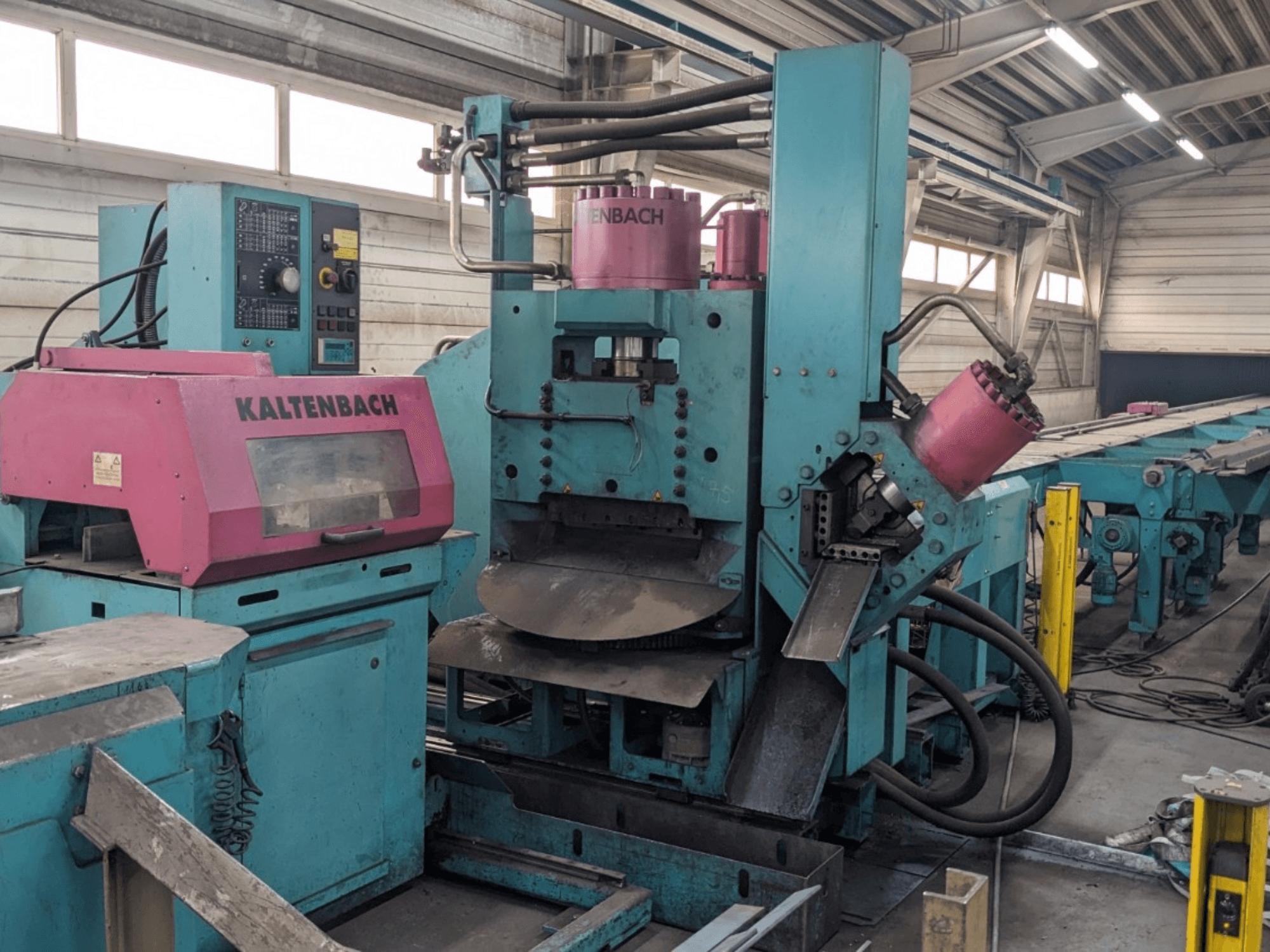 Machine industrielle KALTENBACH de couleur sarcelle et rose, vue de face, avec panneau de commande et composants hydrauliques.