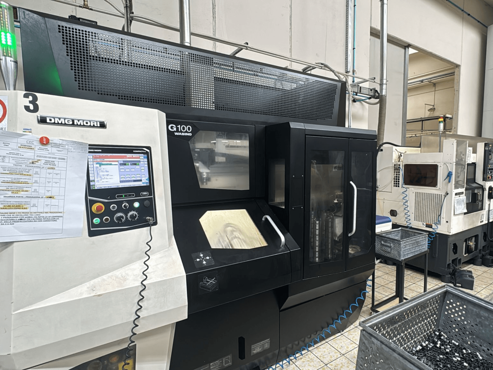 Machine DMG MORI G100 dans une usine, vue de face, avec un panneau de commande numérique et des bacs de stockage d'outils à proximité.