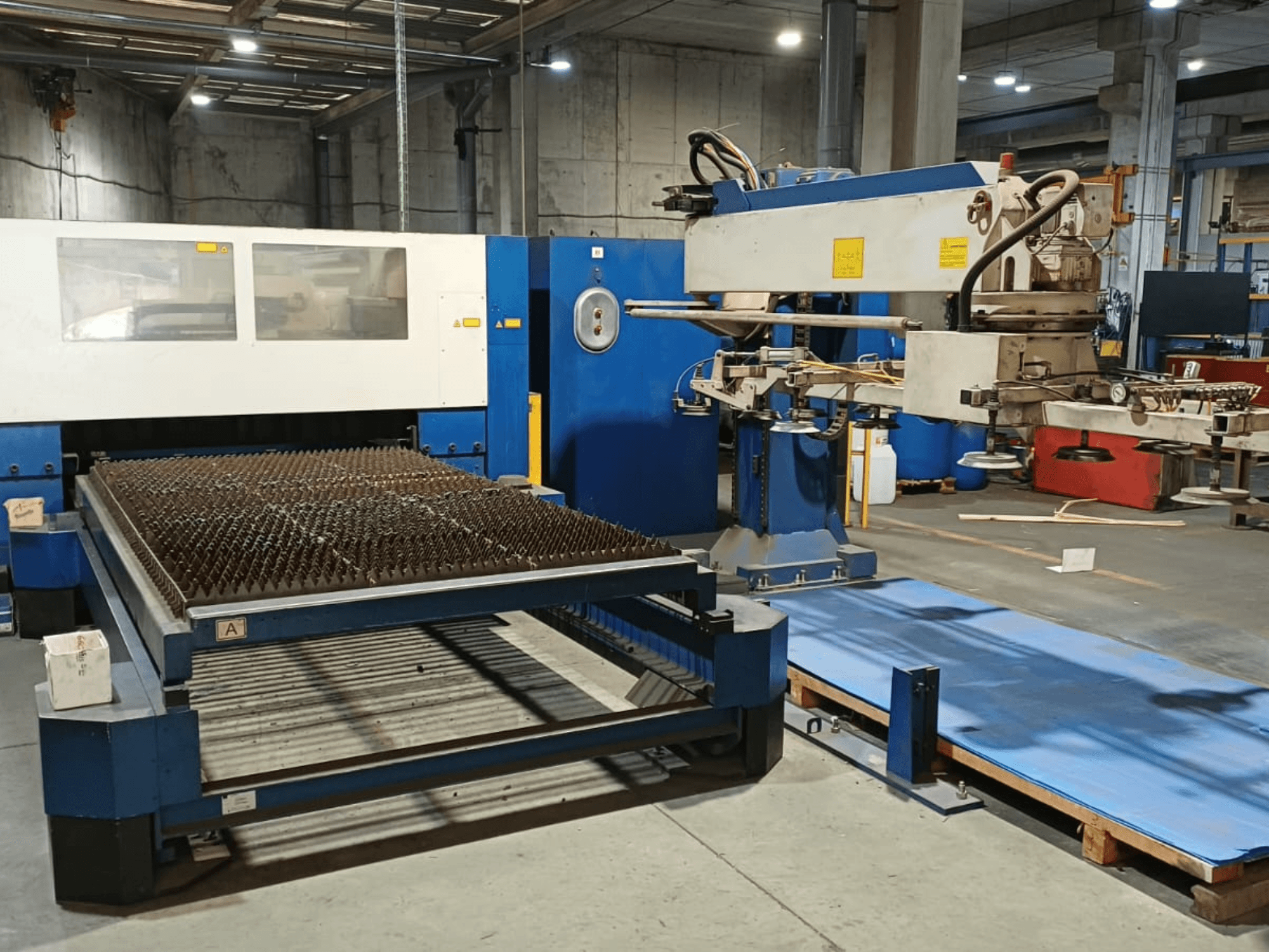 Machine de découpe laser CO₂ TRUMPF TRUMATIC L 3030, vue de profil, mettant en évidence la table de découpe à surface cloutée et le bras robotisé.