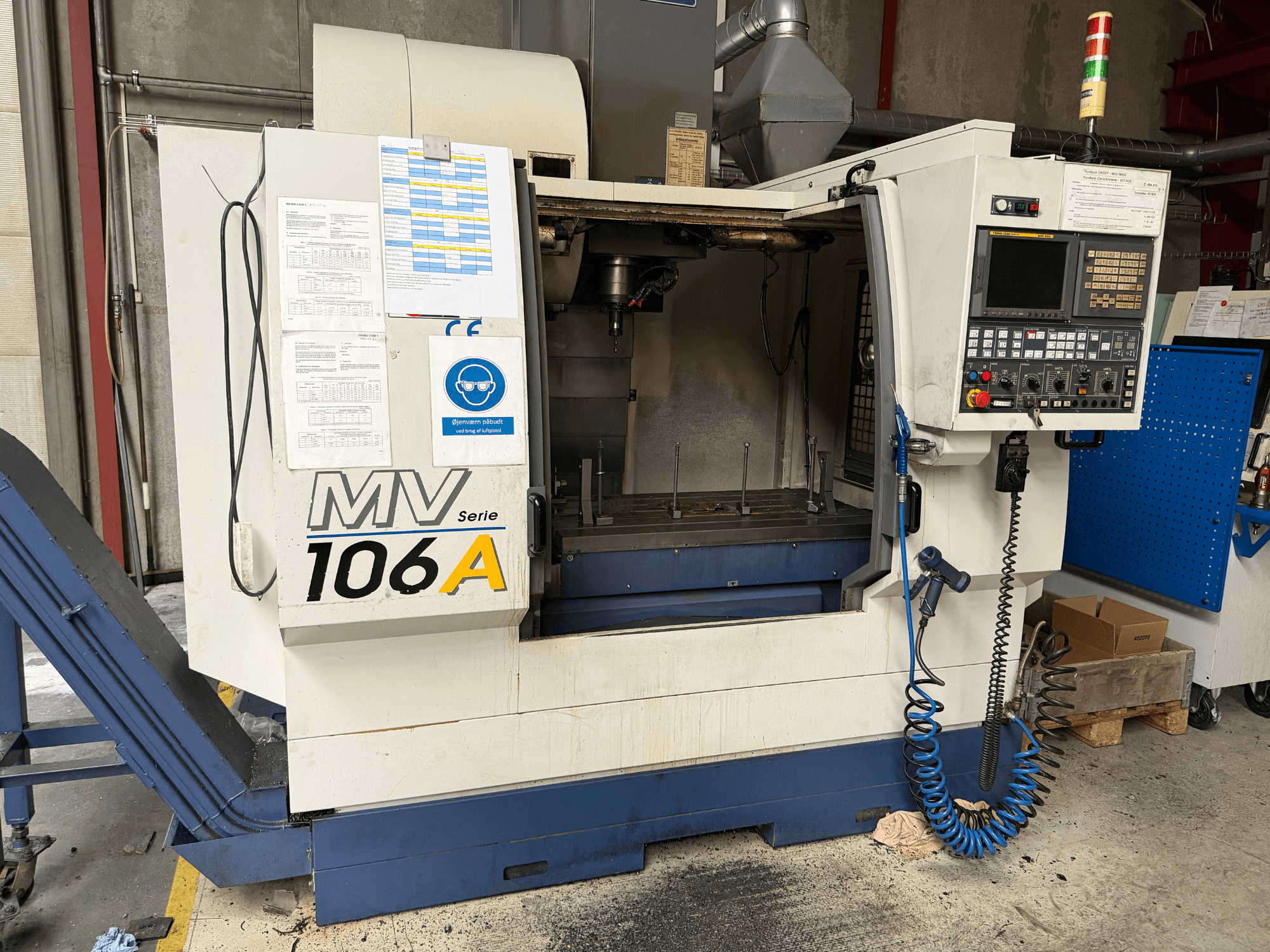 Centre d'usinage vertical YCM MV106A, vue de face montrant le panneau de commande et la zone de travail, avec la documentation technique jointe.