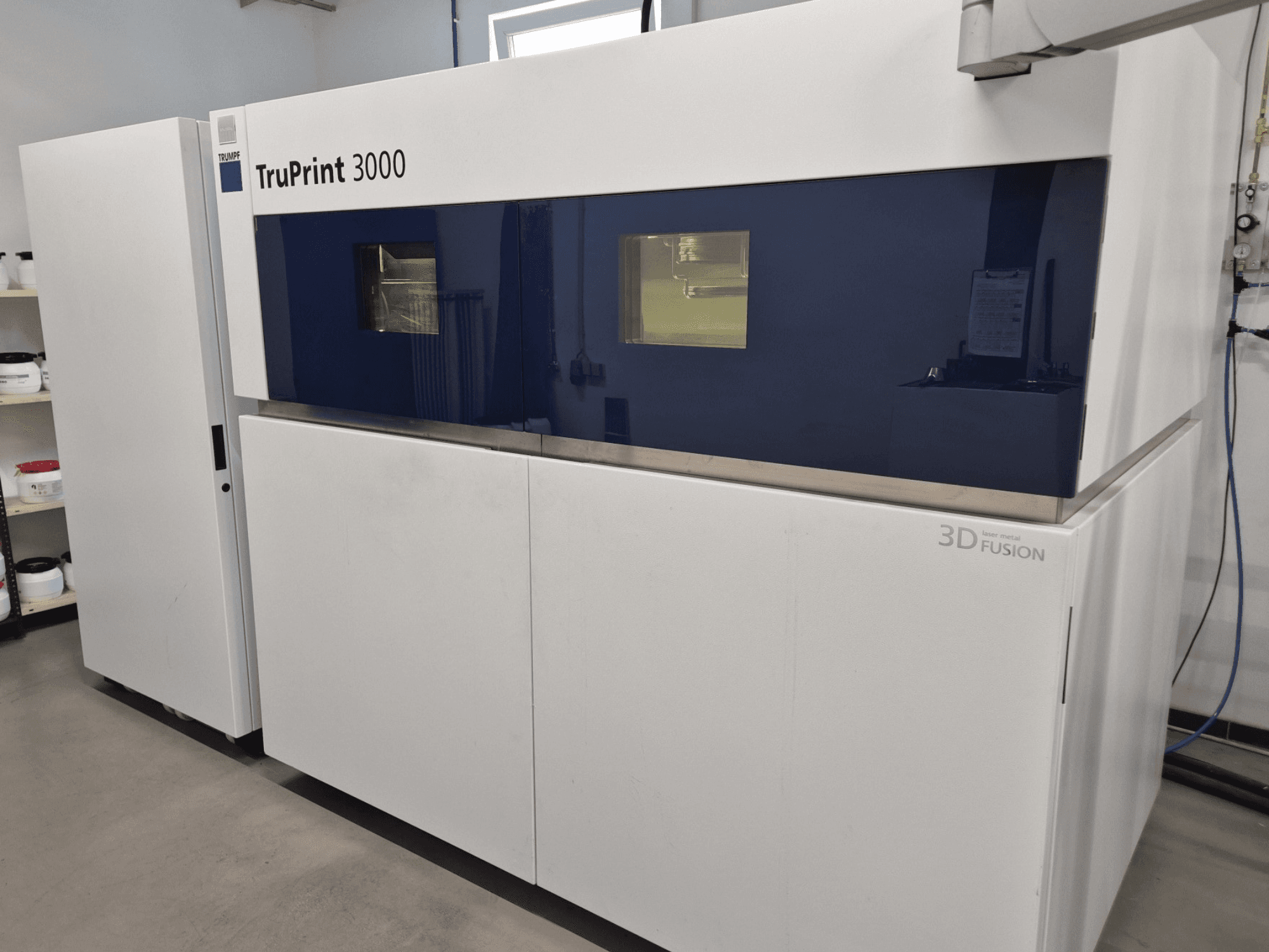 Imprimante 3D TruPrint 3000 métal vue de face, avec un design à panneaux bleus et une technologie de fusion laser.