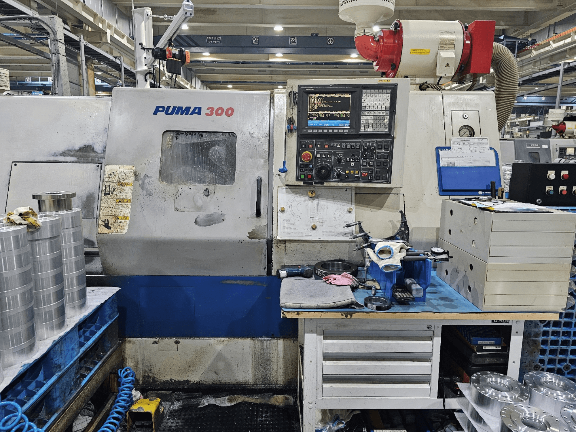 Machine CNC PUMA 300 dans un atelier ; vue de face montrant le panneau de commande, les outils et les pièces métalliques sur un établi.